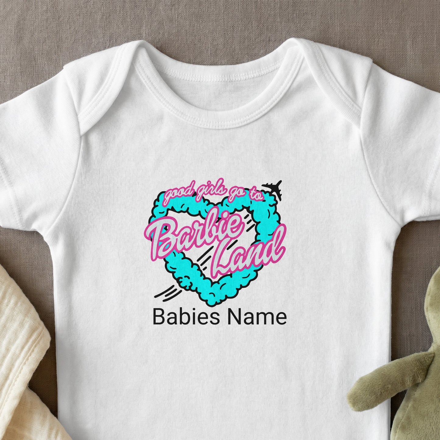 White baby onesie with "Barbie Land" and heart cloud graphic.