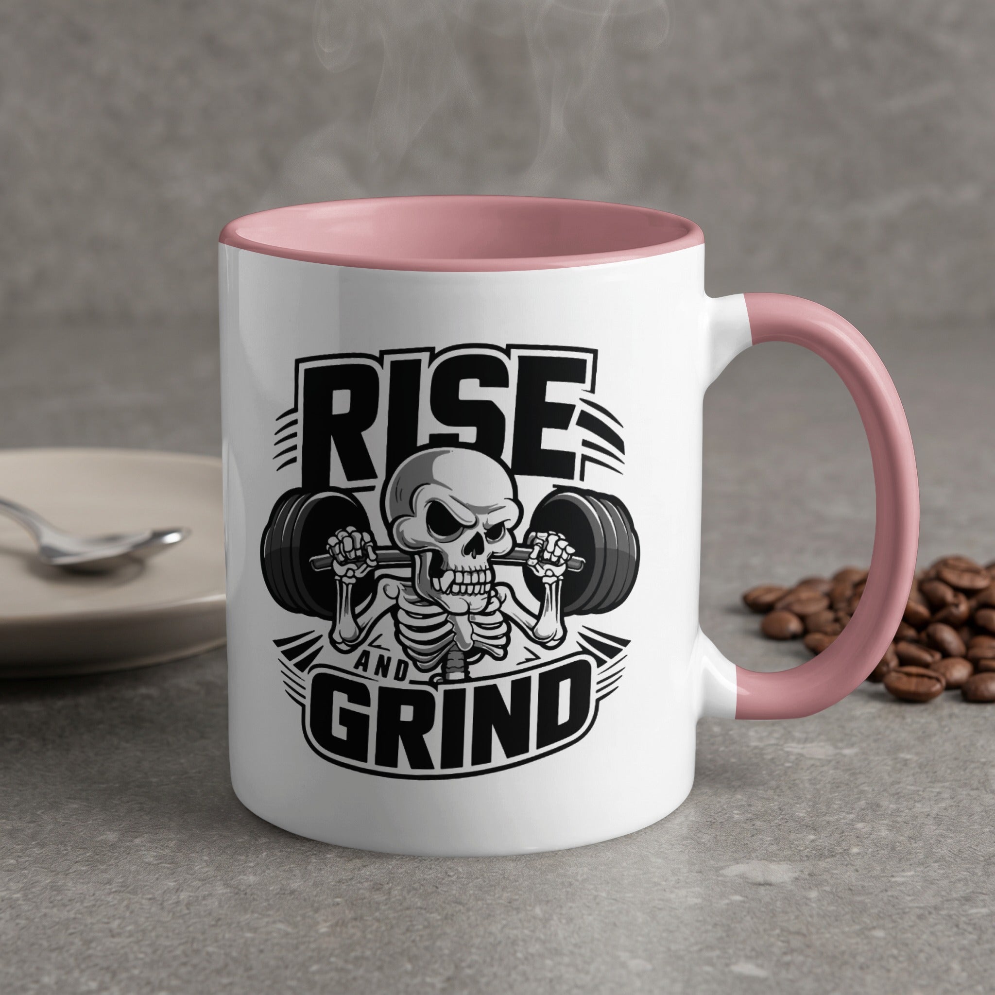 White mug with pink handle and "Rise and Grind" skeleton lifting weights graphic.
