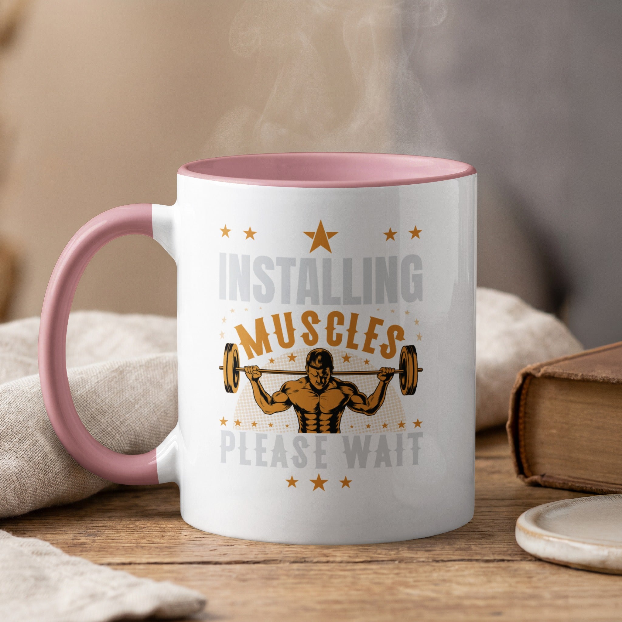 White mug with pink handle, steaming, features "Installing Muscles Please Wait" and barbell graphic.
