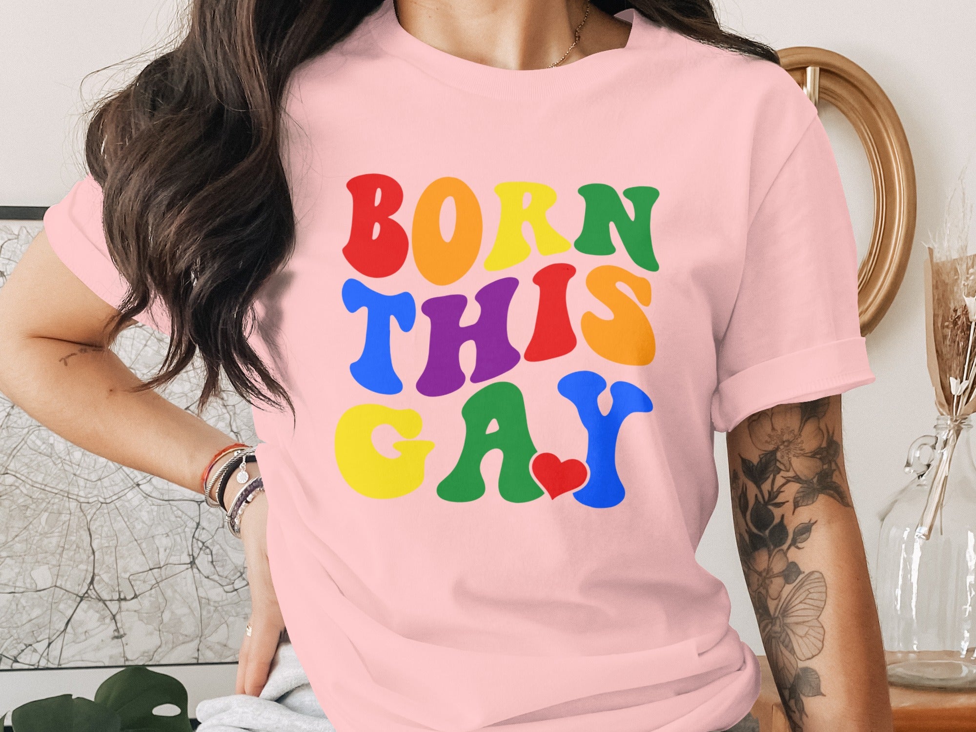 Pink t-shirt with "BORN THIS GAY" in colorful, groovy font, small red heart.