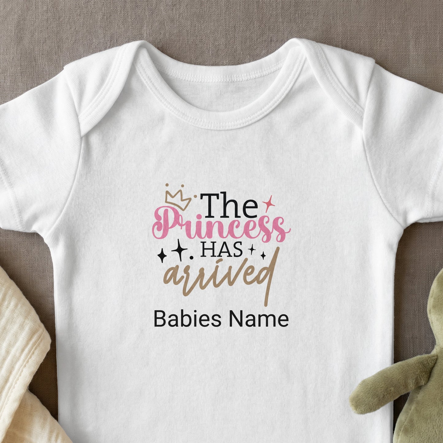 White baby onesie with "The Princess Has Arrived" text and crown graphic.