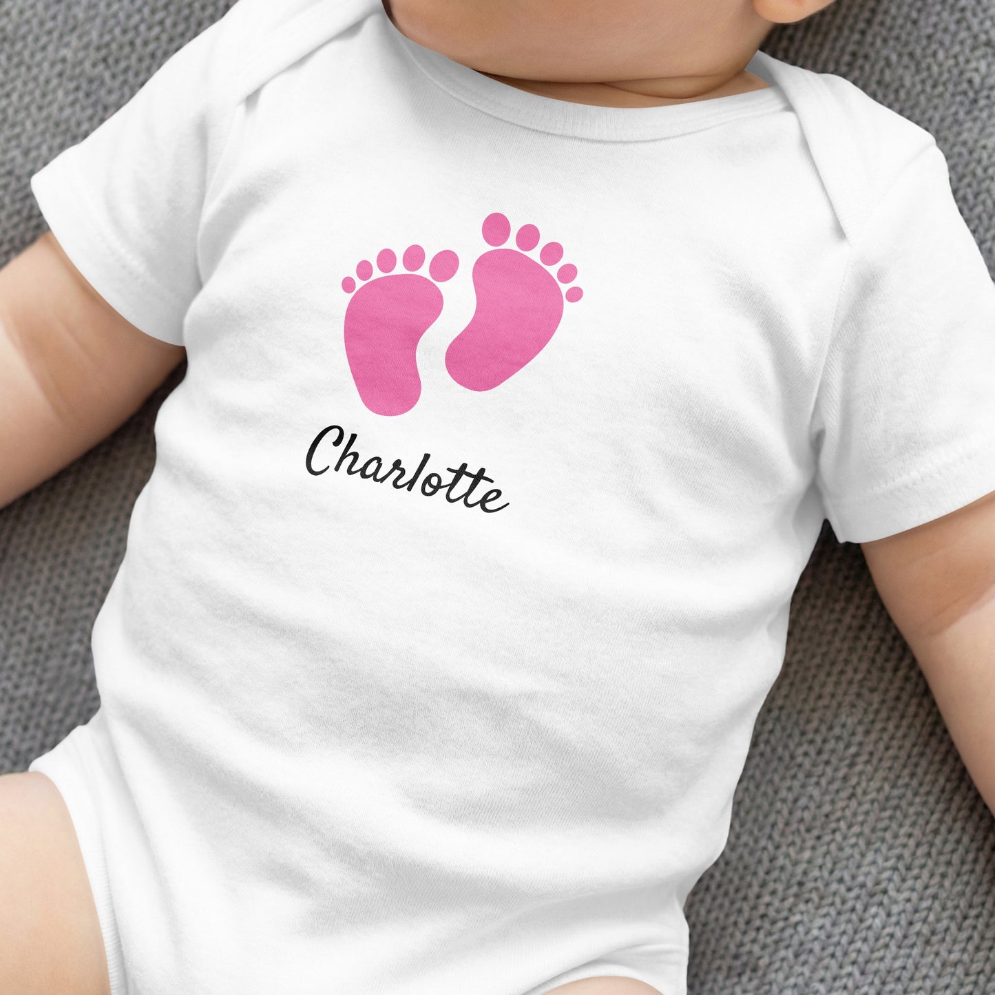 White baby onesie with pink footprints and "Charlotte" text.