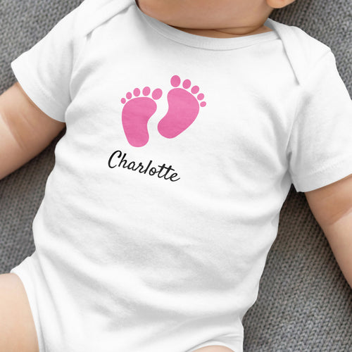 White baby onesie with pink footprints and "Charlotte" text.