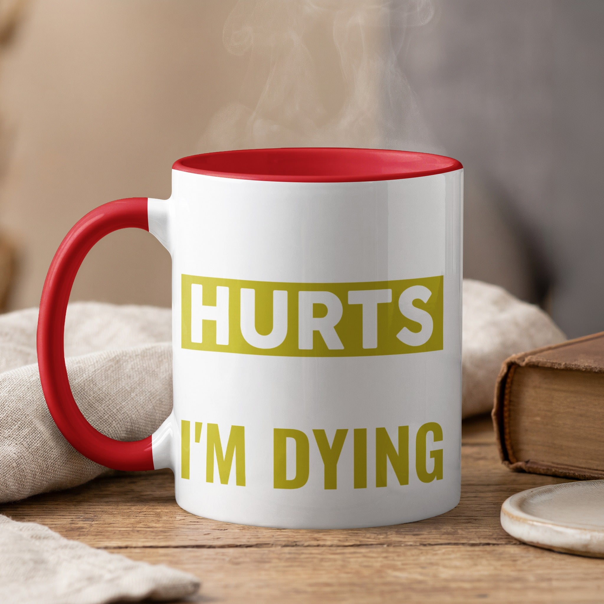 Red-handled mug with "HURTS I'M DYING" text, emitting steam.