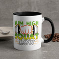 White mug with "Aim High Squat Low" text and dumbbell graphics.