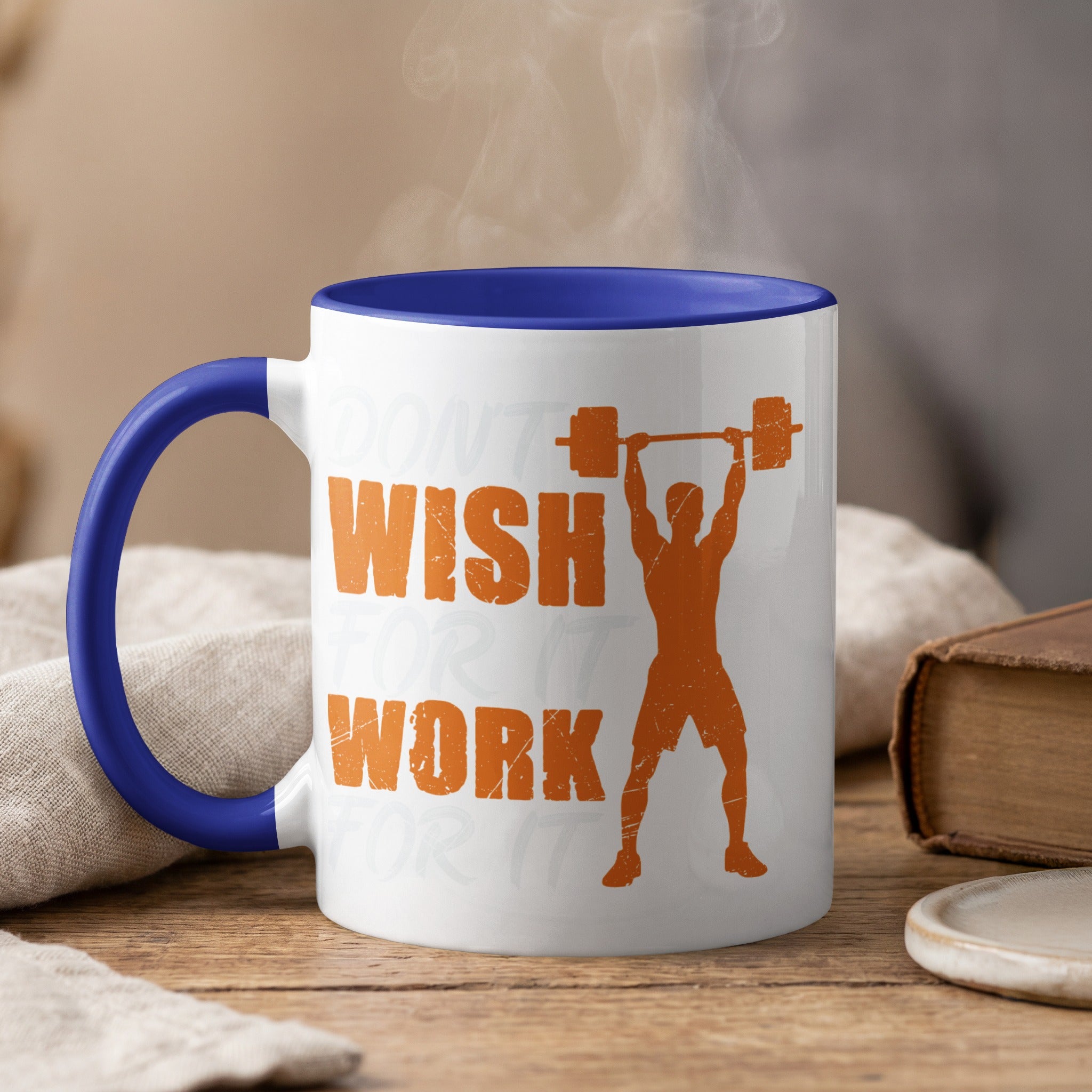 White mug with blue rim, steam rising, features orange text and barbell lifting graphic.
