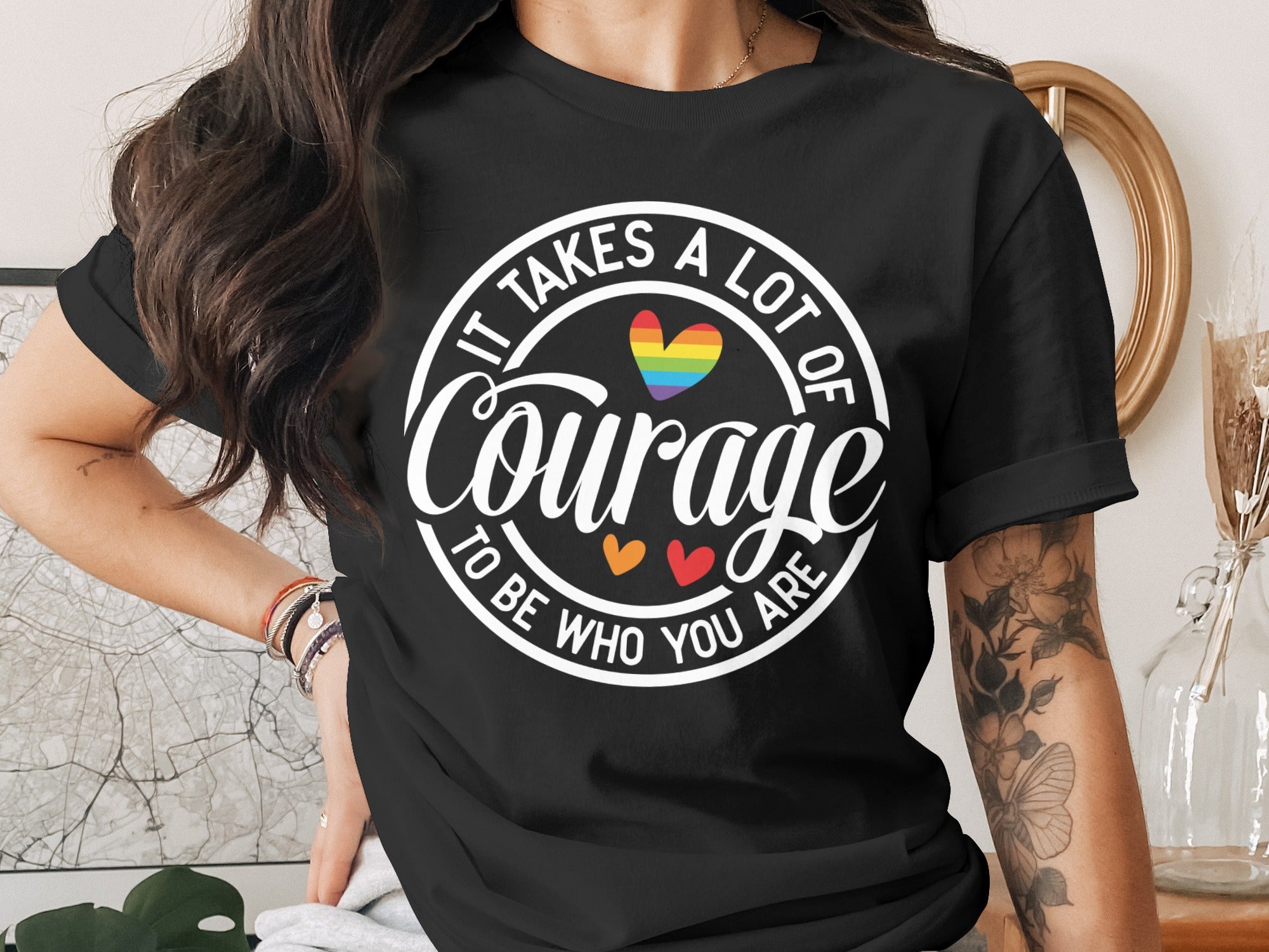 Black t-shirt with white text "IT TAKES A LOT OF COURAGE TO BE WHO YOU ARE" and rainbow heart.