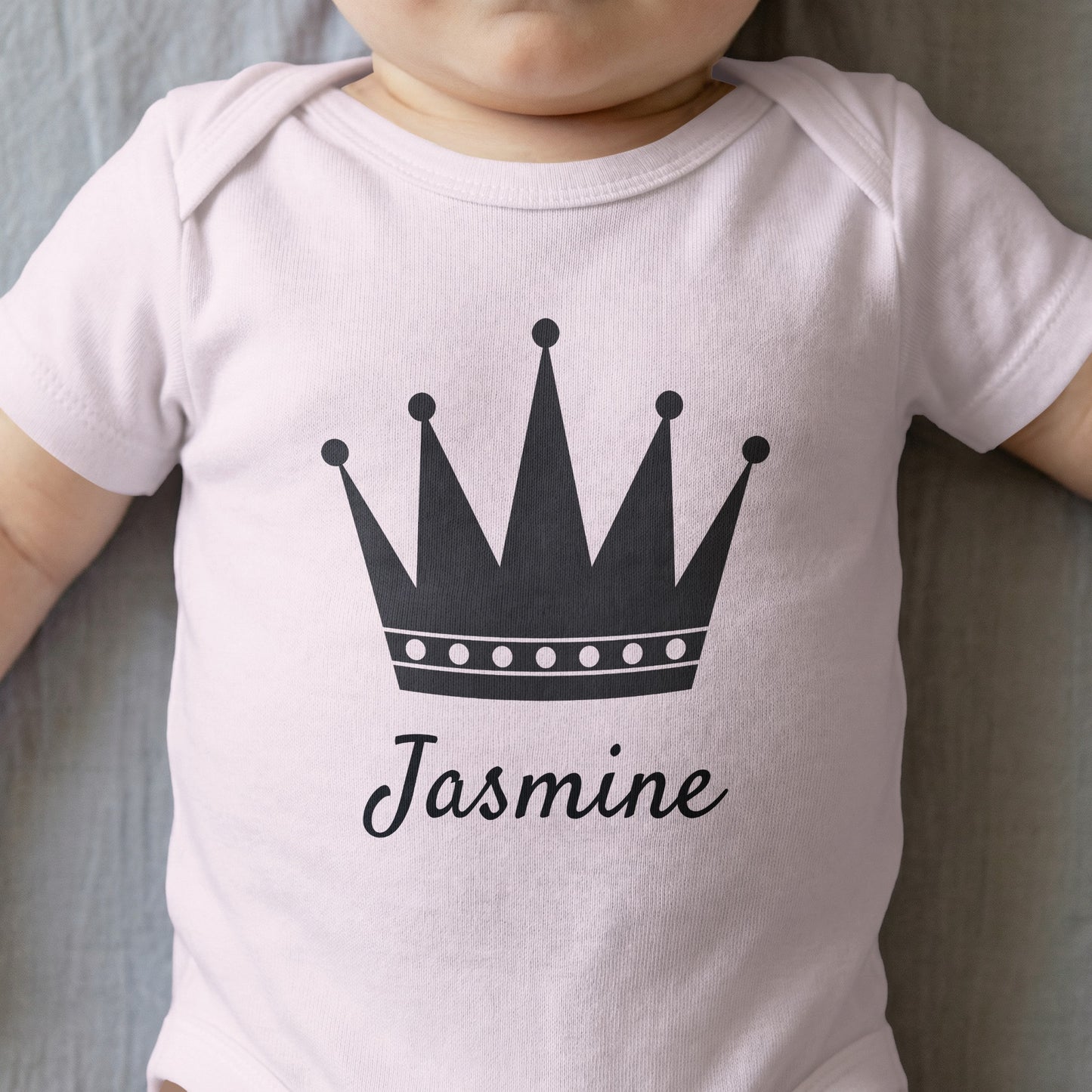 White baby onesie with a dark crown and "Jasmine" printed on it.