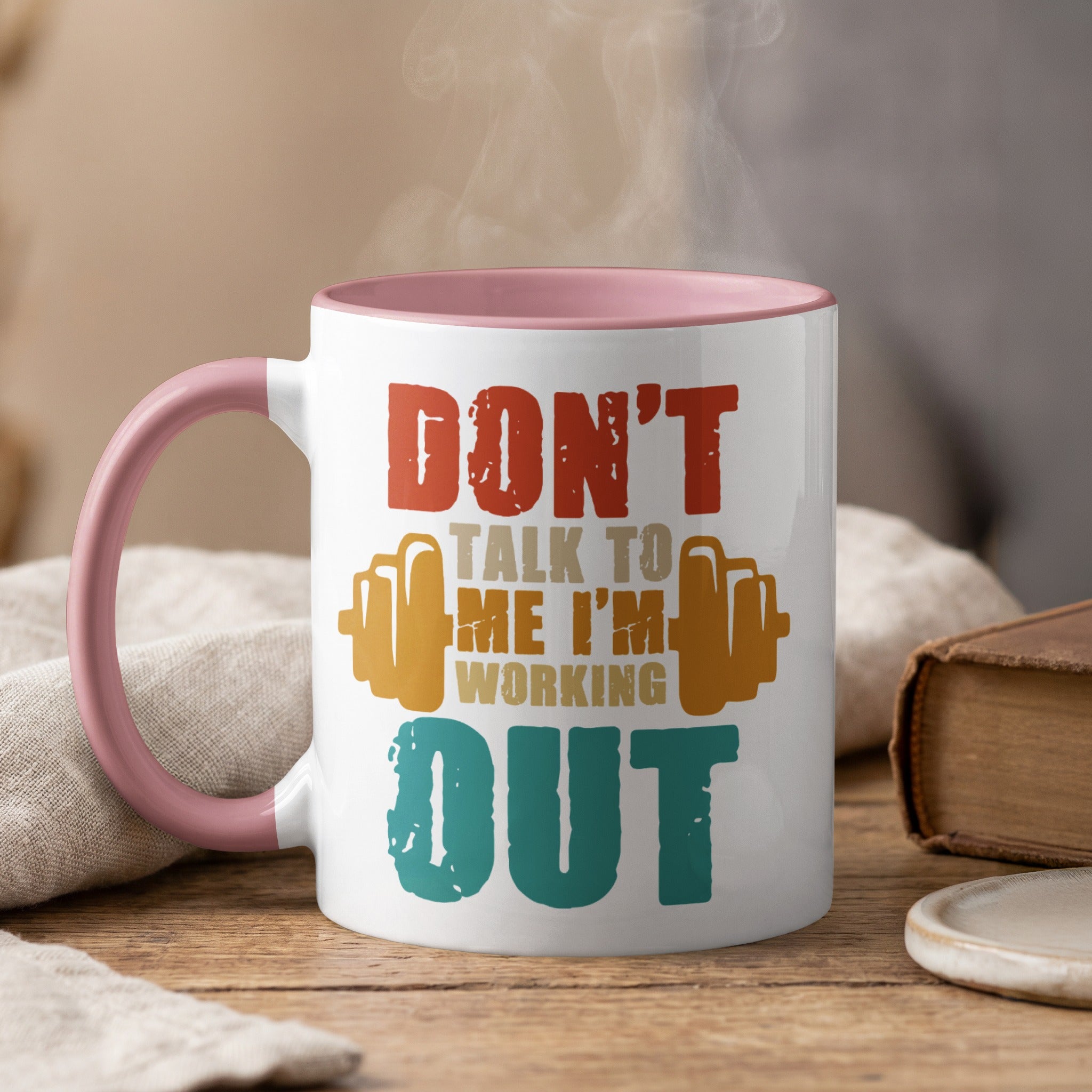White mug with pink handle, "DON'T TALK TO ME I'M WORKING OUT" text and barbell graphic.