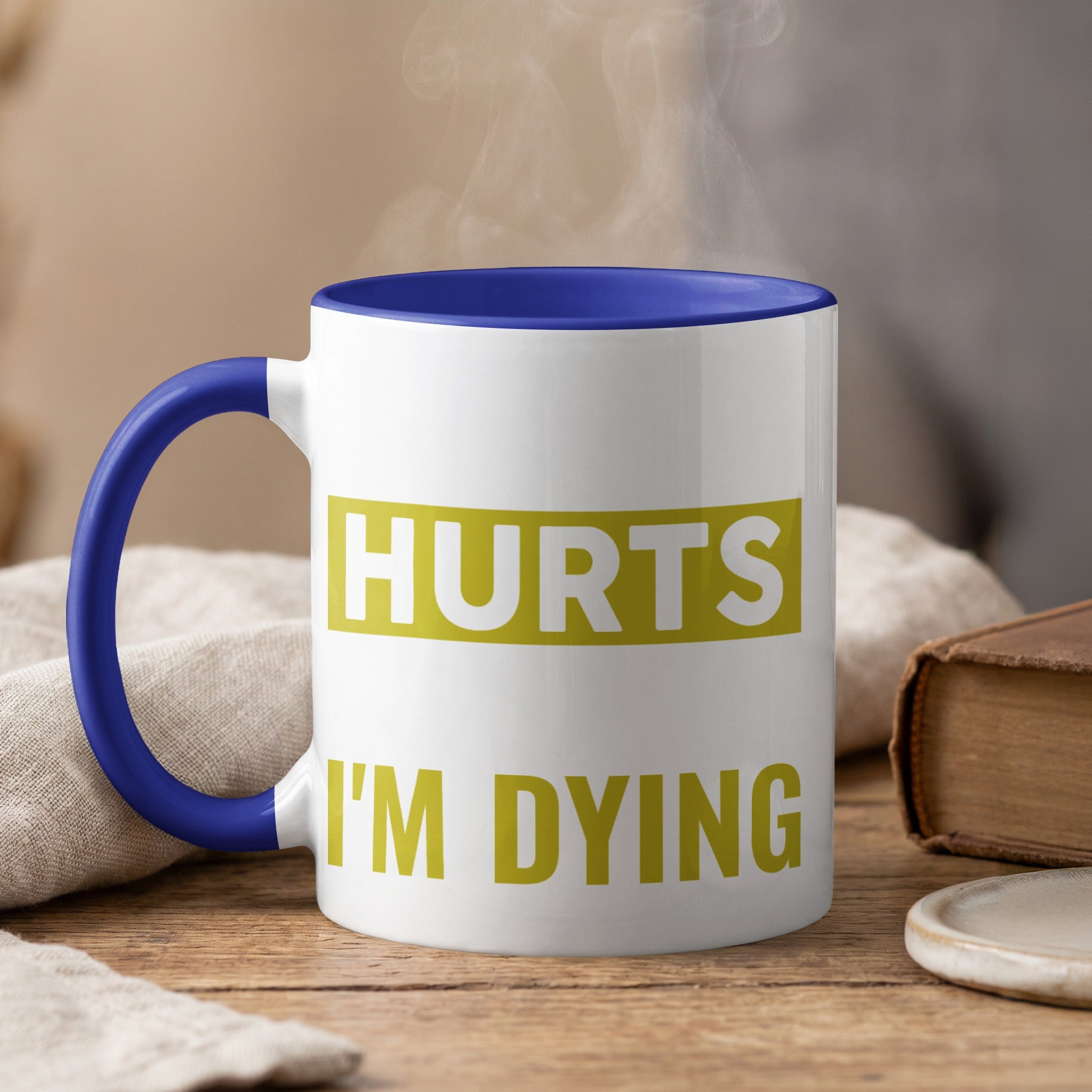 White mug with blue handle, text "HURTS I'M DYING" in yellow.