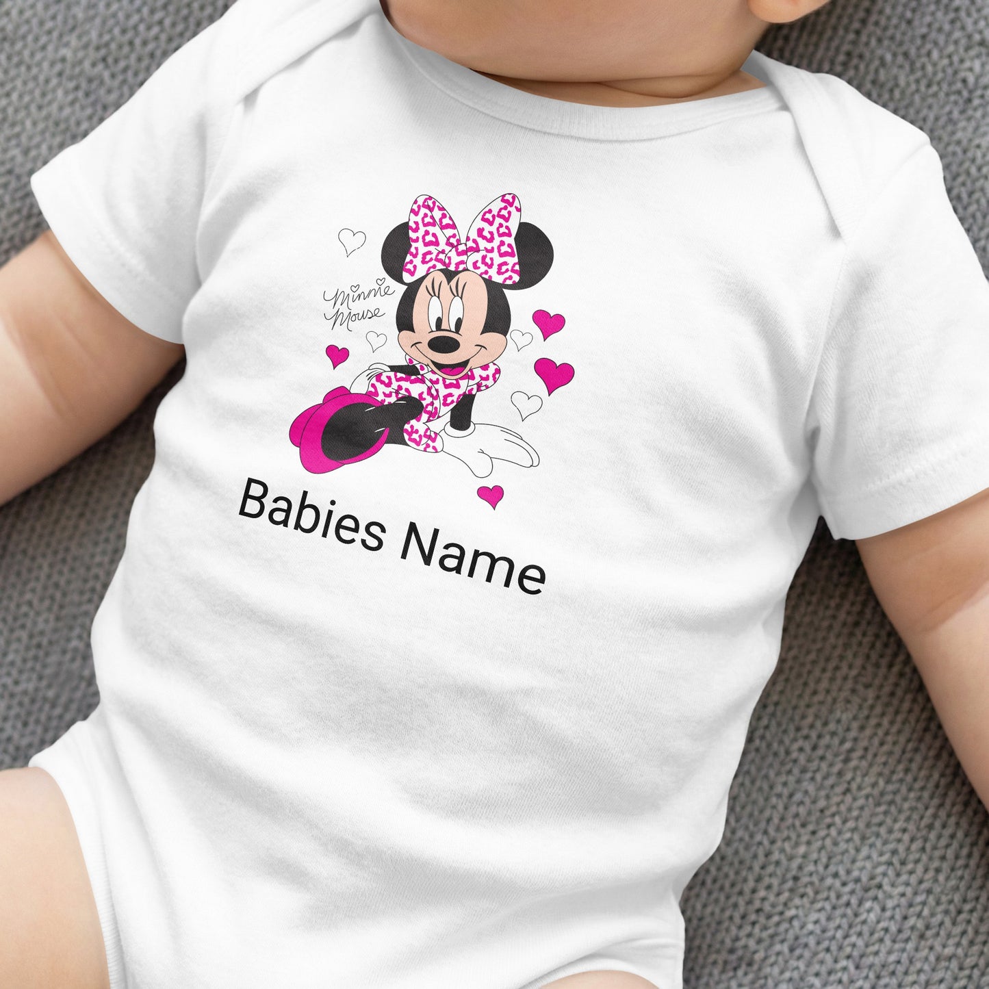 White baby onesie with Minnie Mouse, pink bow, and customizable "Babies Name".