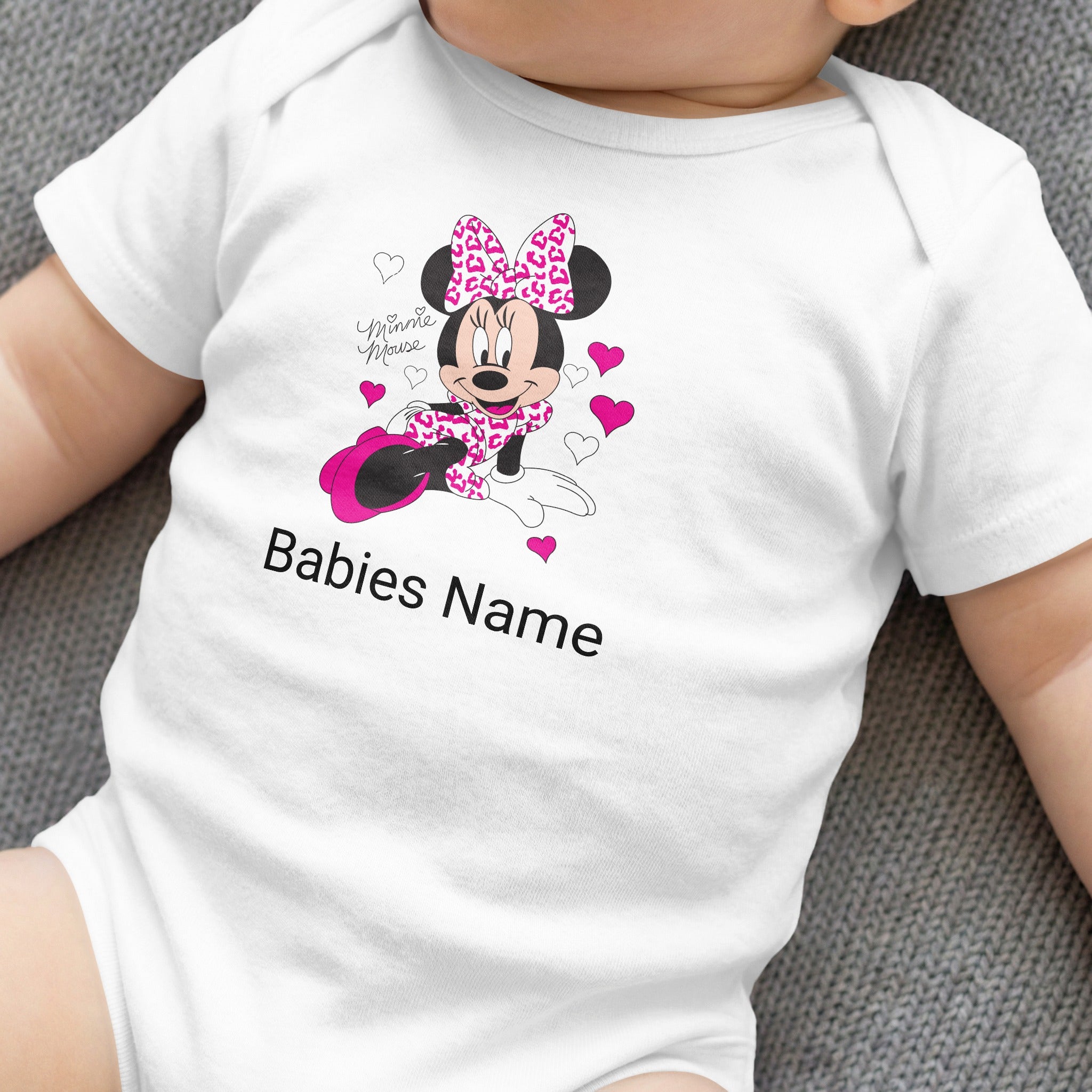 White baby onesie with Minnie Mouse, pink bow, and customizable "Babies Name".