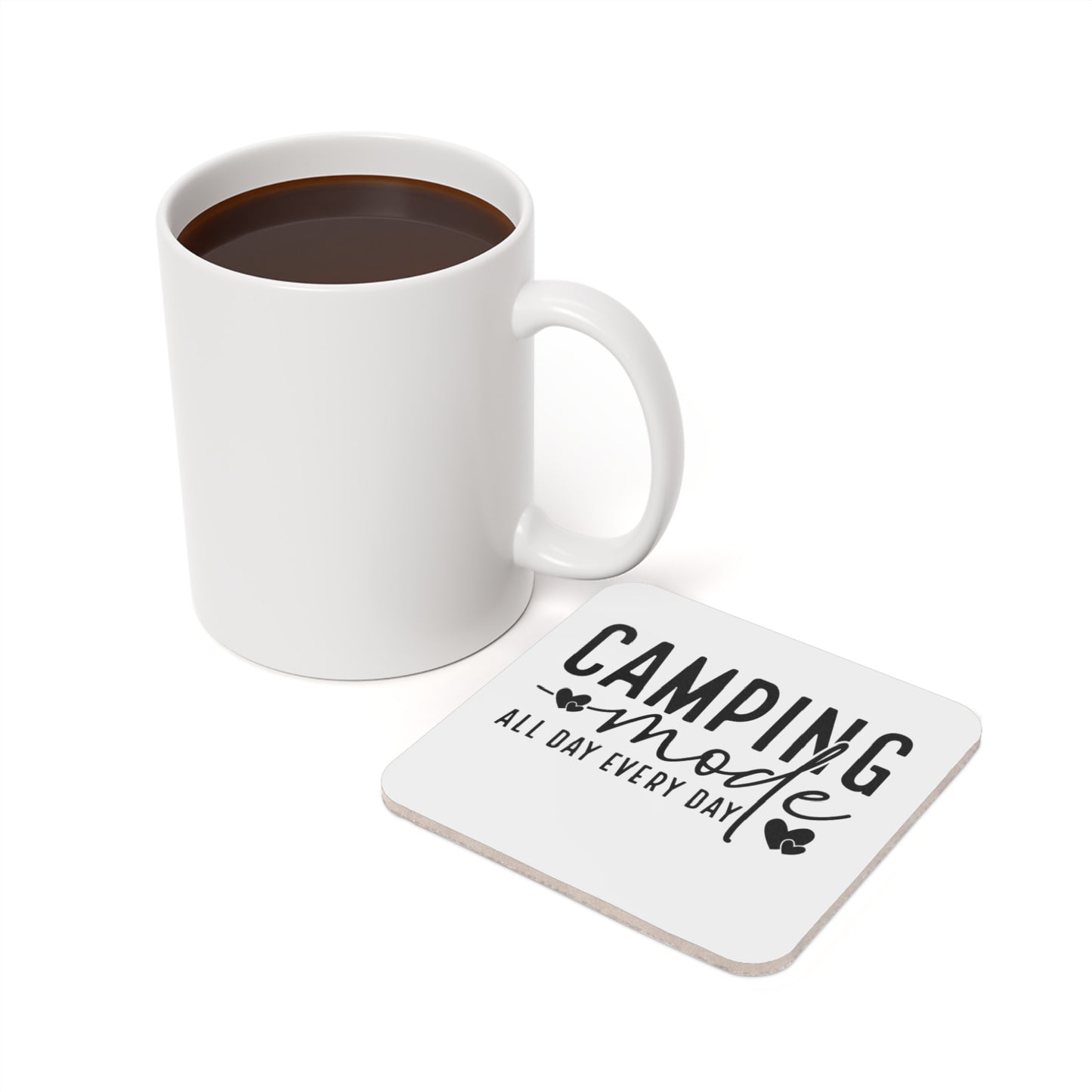 White mug with coffee next to white square coaster that reads "Camping mode all day every day".