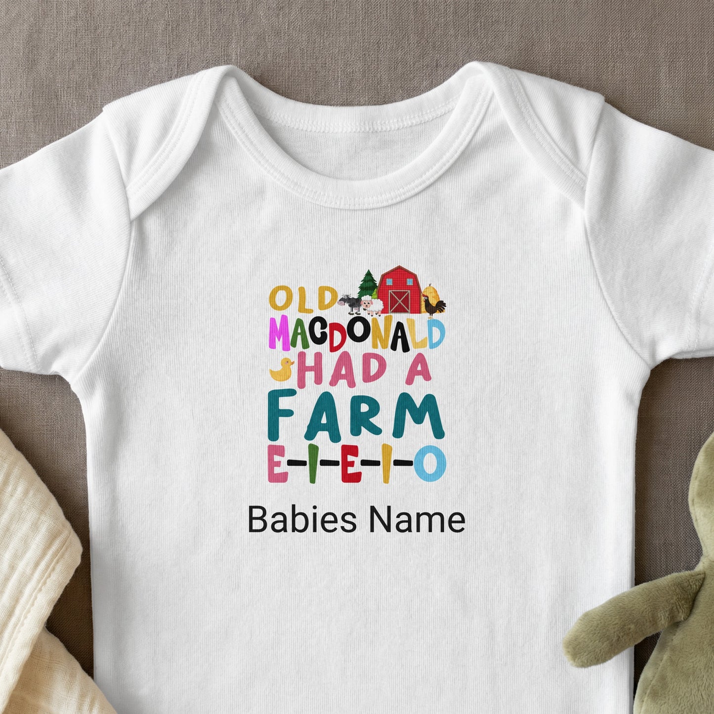 White baby onesie with "Old MacDonald Had a Farm" lyrics and colorful barn illustration.