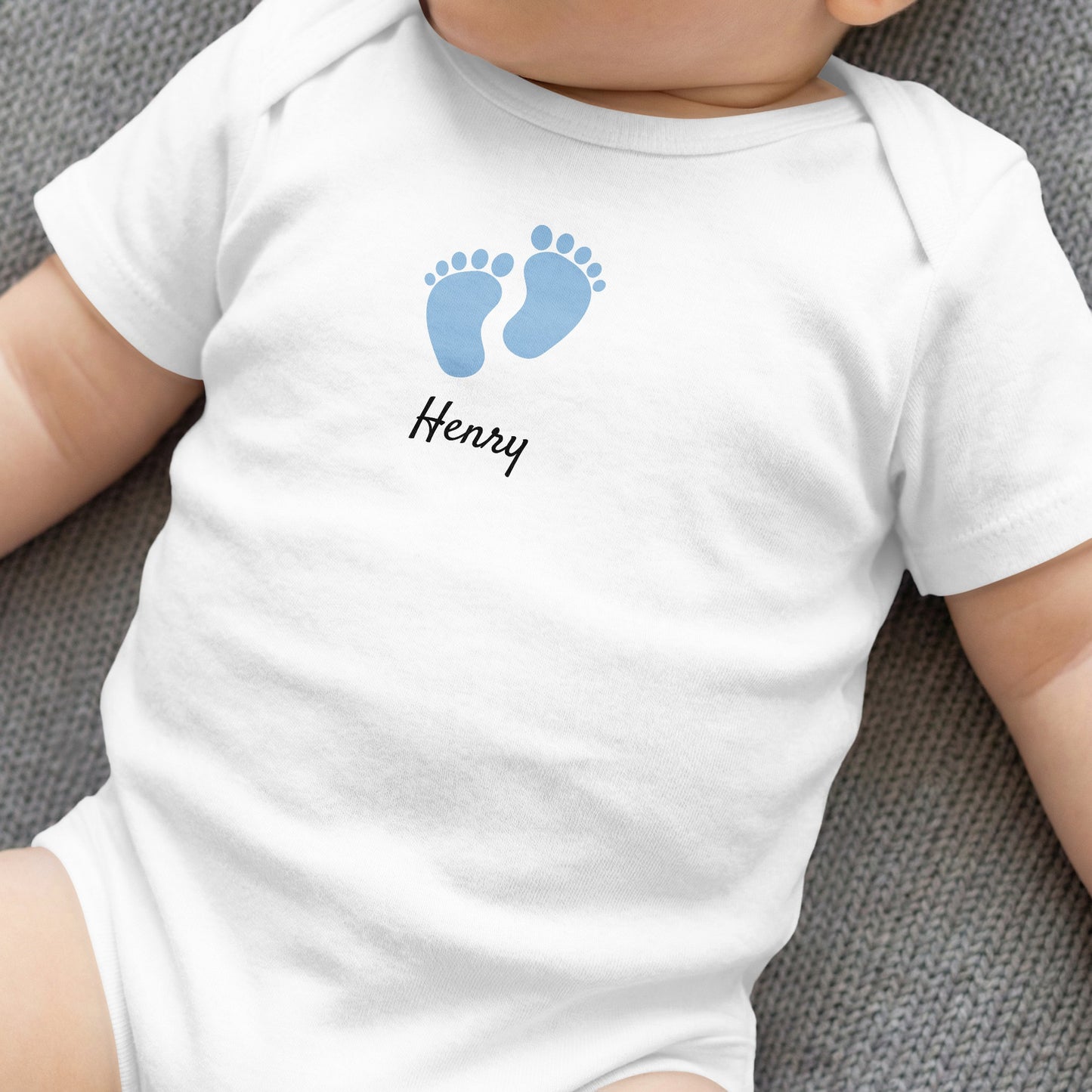 White baby onesie with blue footprints and "Henry" text.
