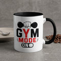 White mug with black rim, "GYM MODE ON" text and dumbbell graphic.