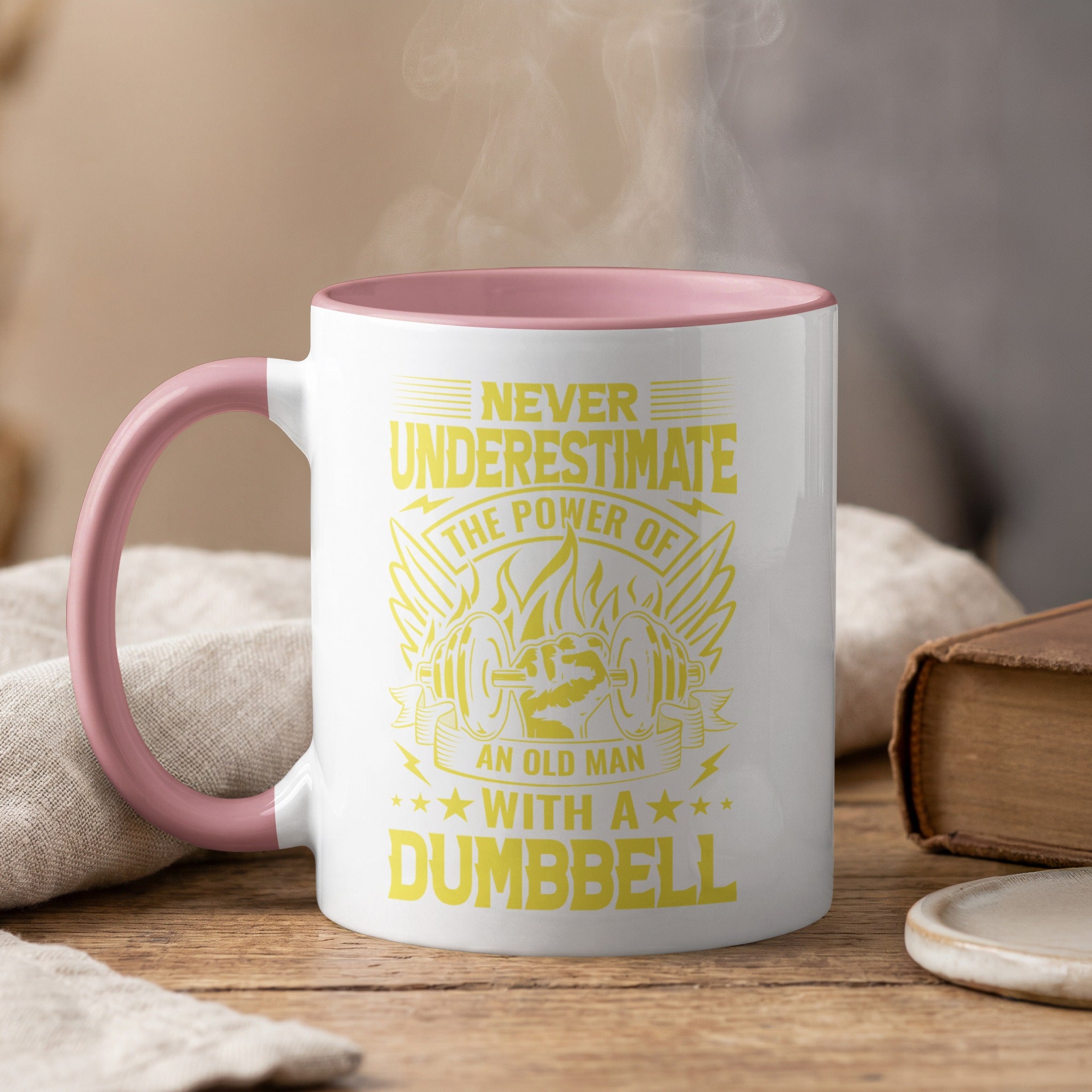Mug with pink rim and handle, featuring yellow text and graphics about an old man with a dumbbell.