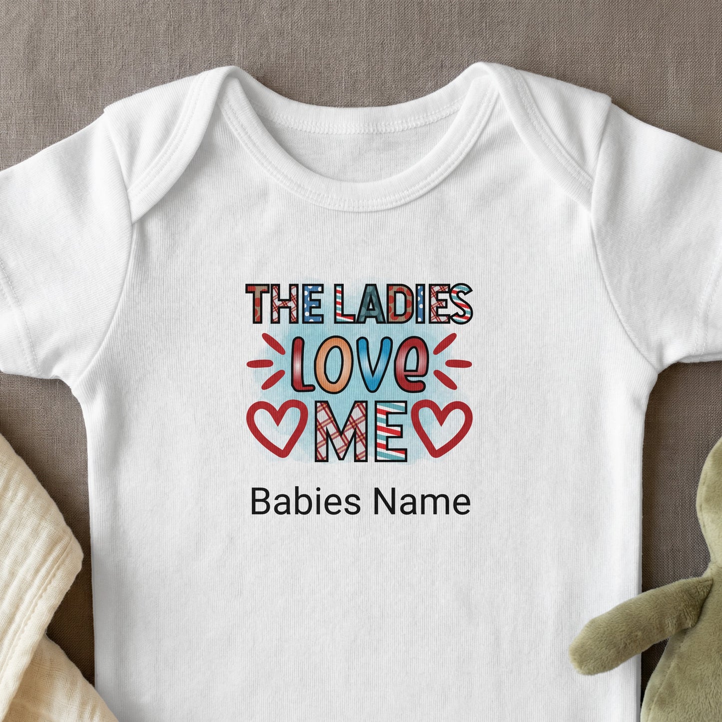 White baby onesie with "The Ladies Love Me" design and space for name.