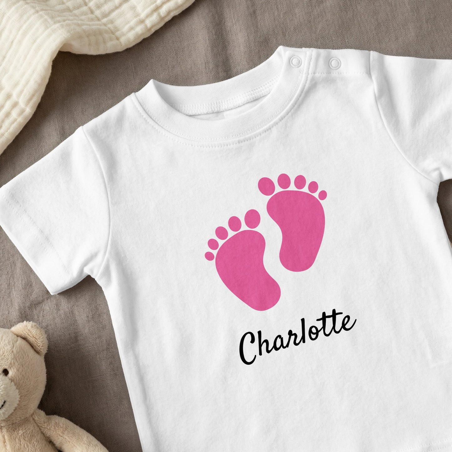 White baby onesie with pink footprints and "Charlotte" text.