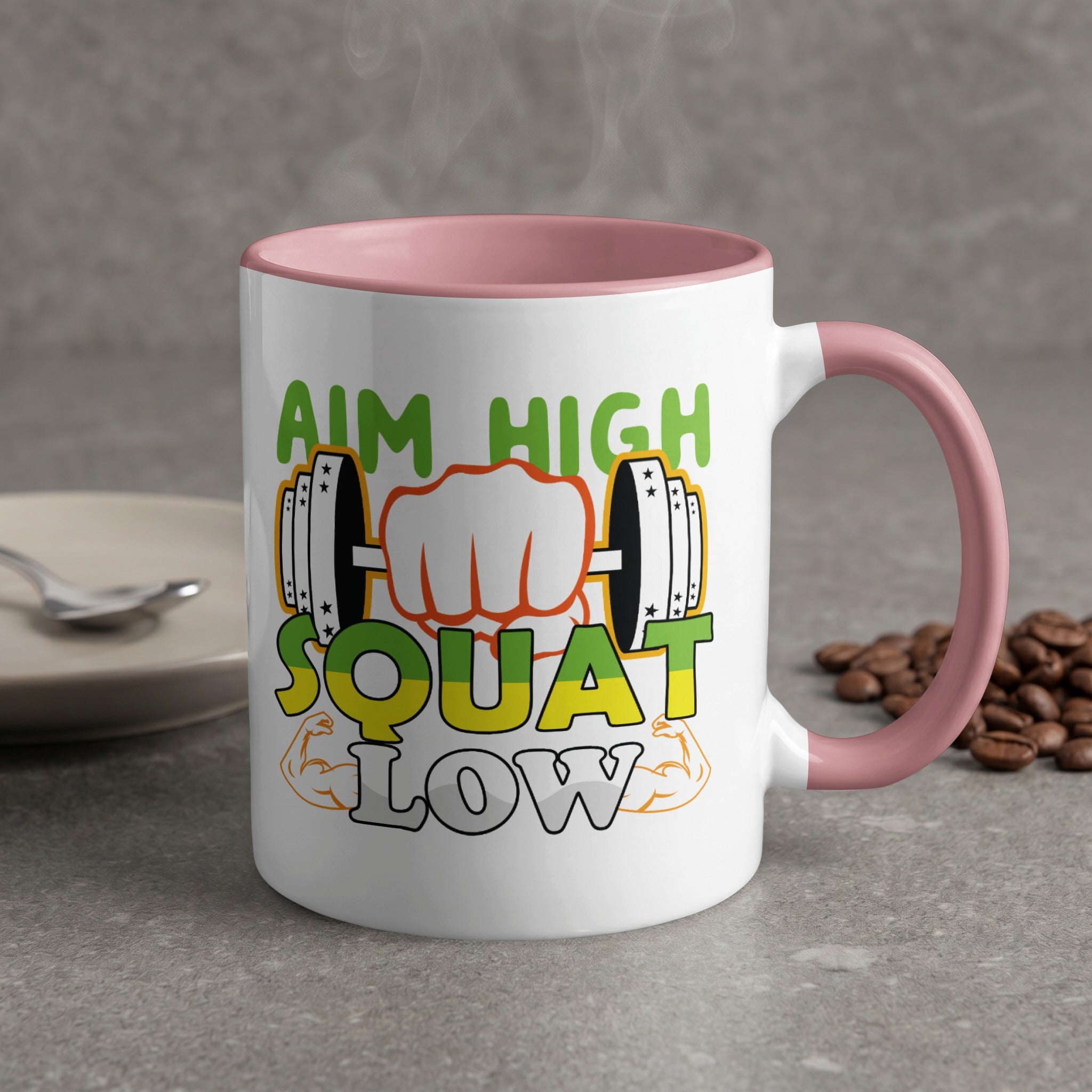White mug with pink handle, text "AIM HIGH SQUAT LOW" and fitness graphics.