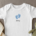 White baby bodysuit with blue footprints and "Henry" text.