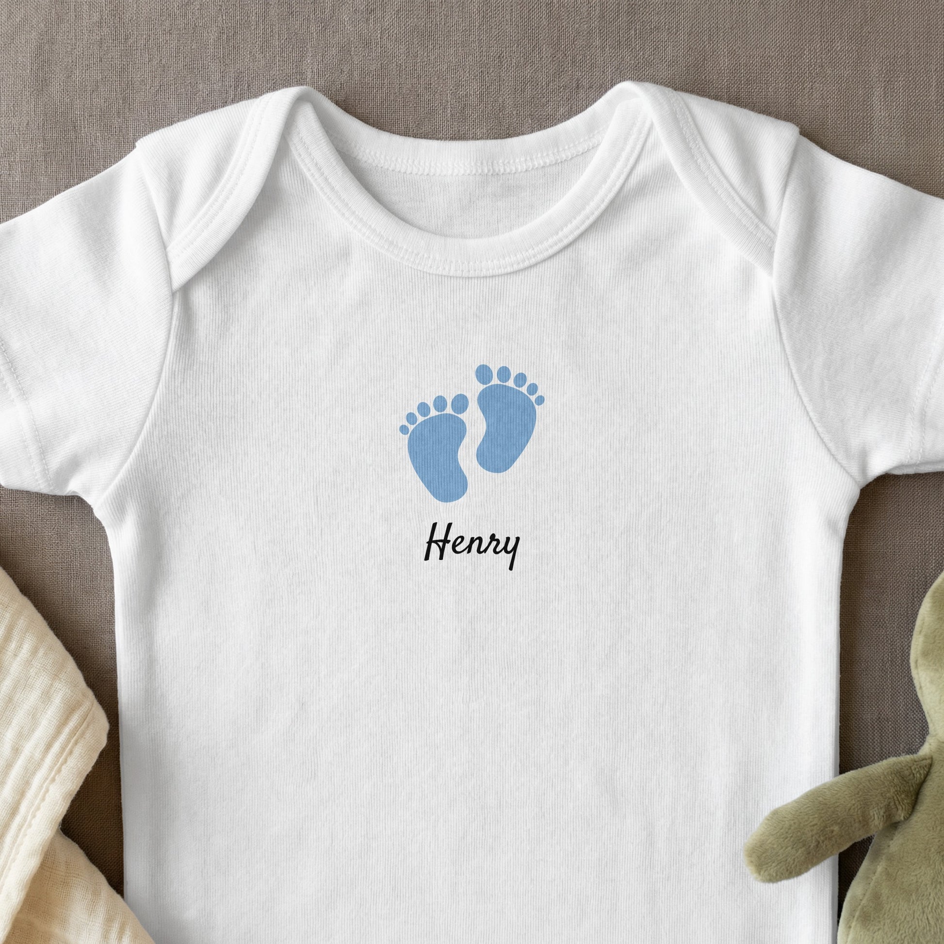 White baby bodysuit with blue footprints and "Henry" text.