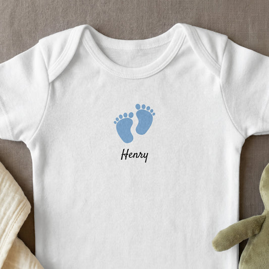 White baby bodysuit with blue footprints and "Henry" text.