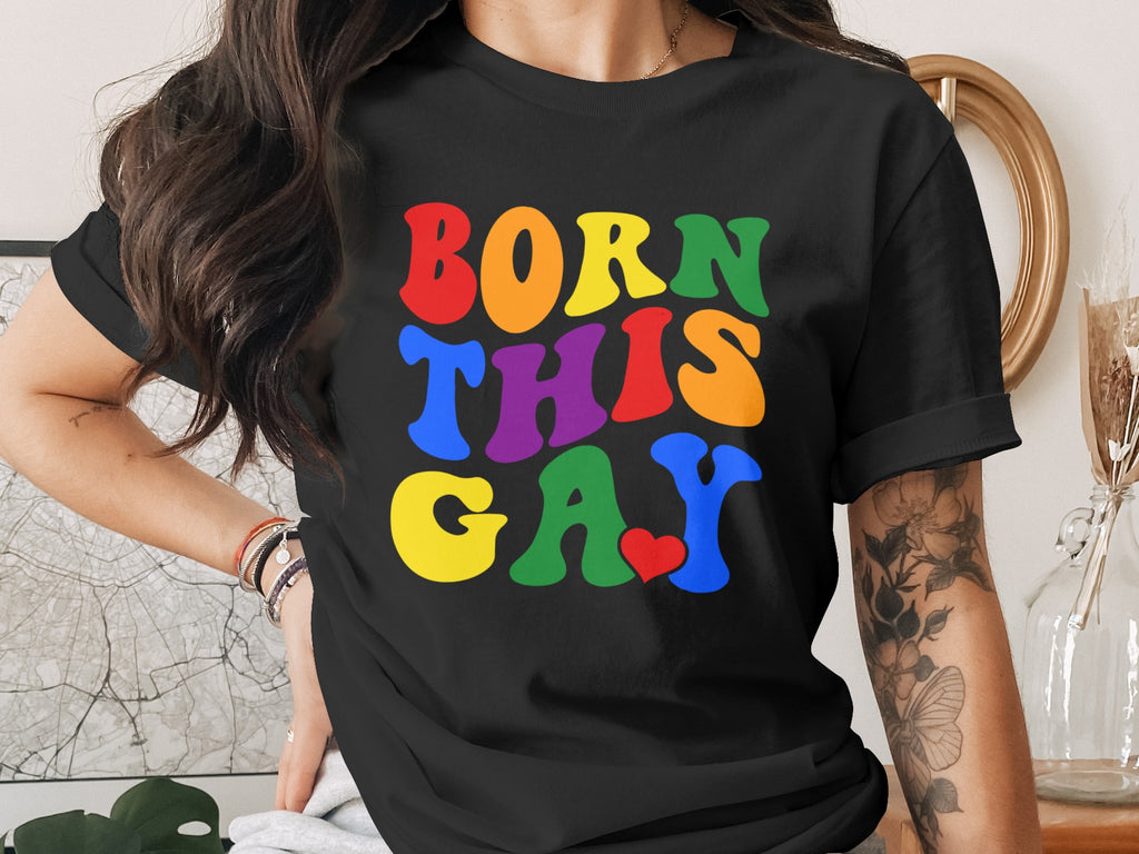 Black t-shirt with "BORN THIS GAY" text in rainbow colors and a small red heart.
