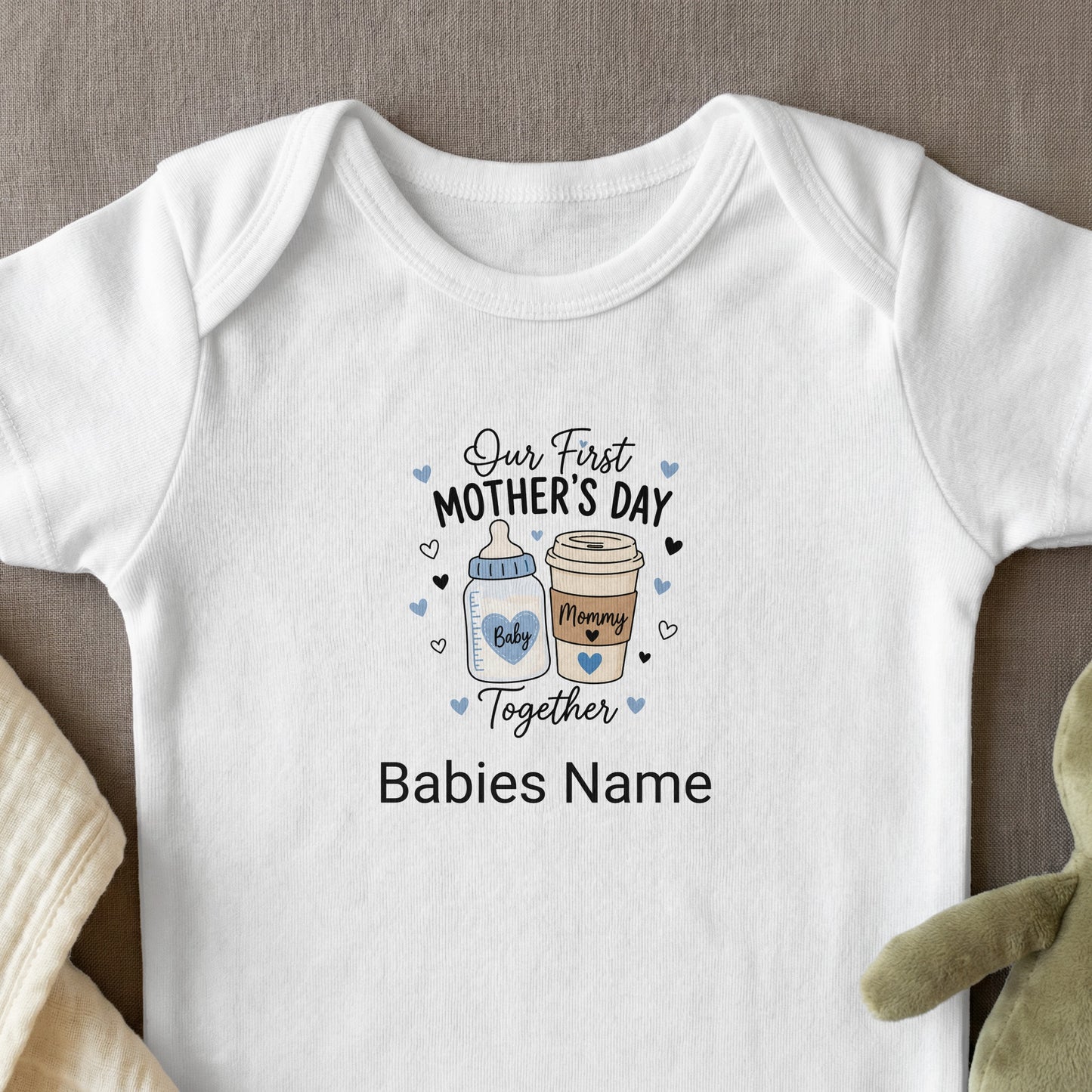 White baby onesie with "Our First Mother's Day Together" text and baby icons.