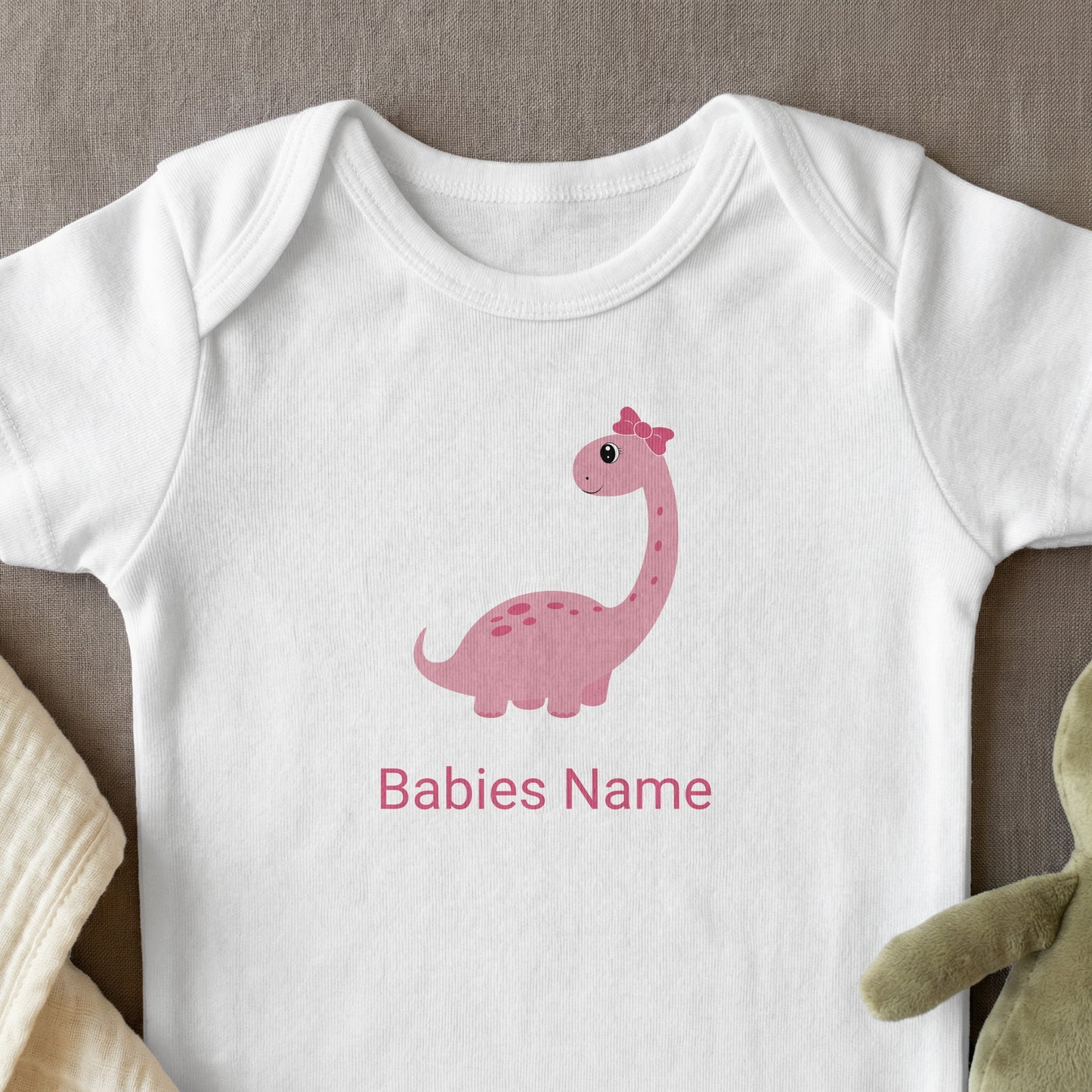 White baby onesie with pink dinosaur graphic and personalized text.