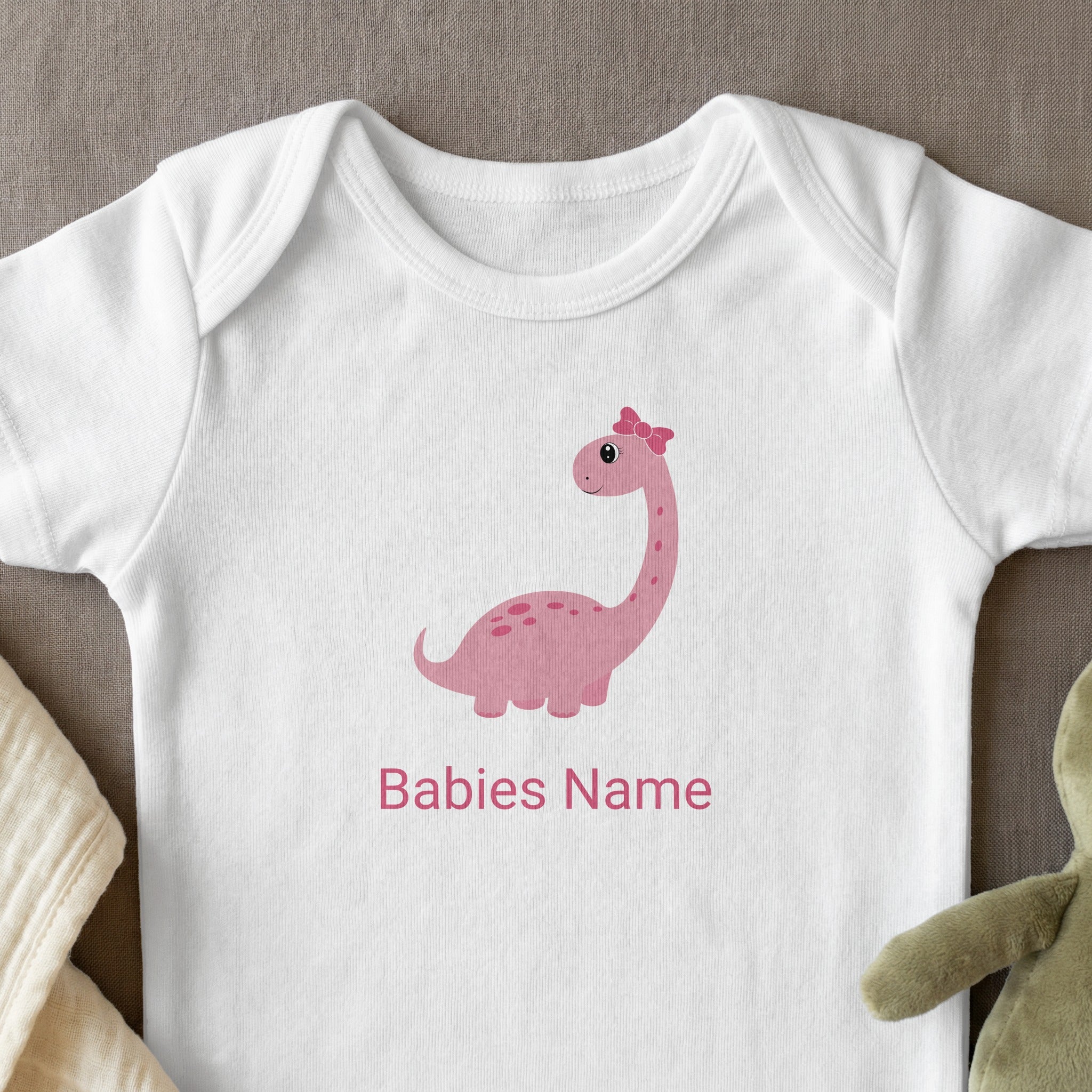 White baby onesie with pink dinosaur graphic and personalized text.