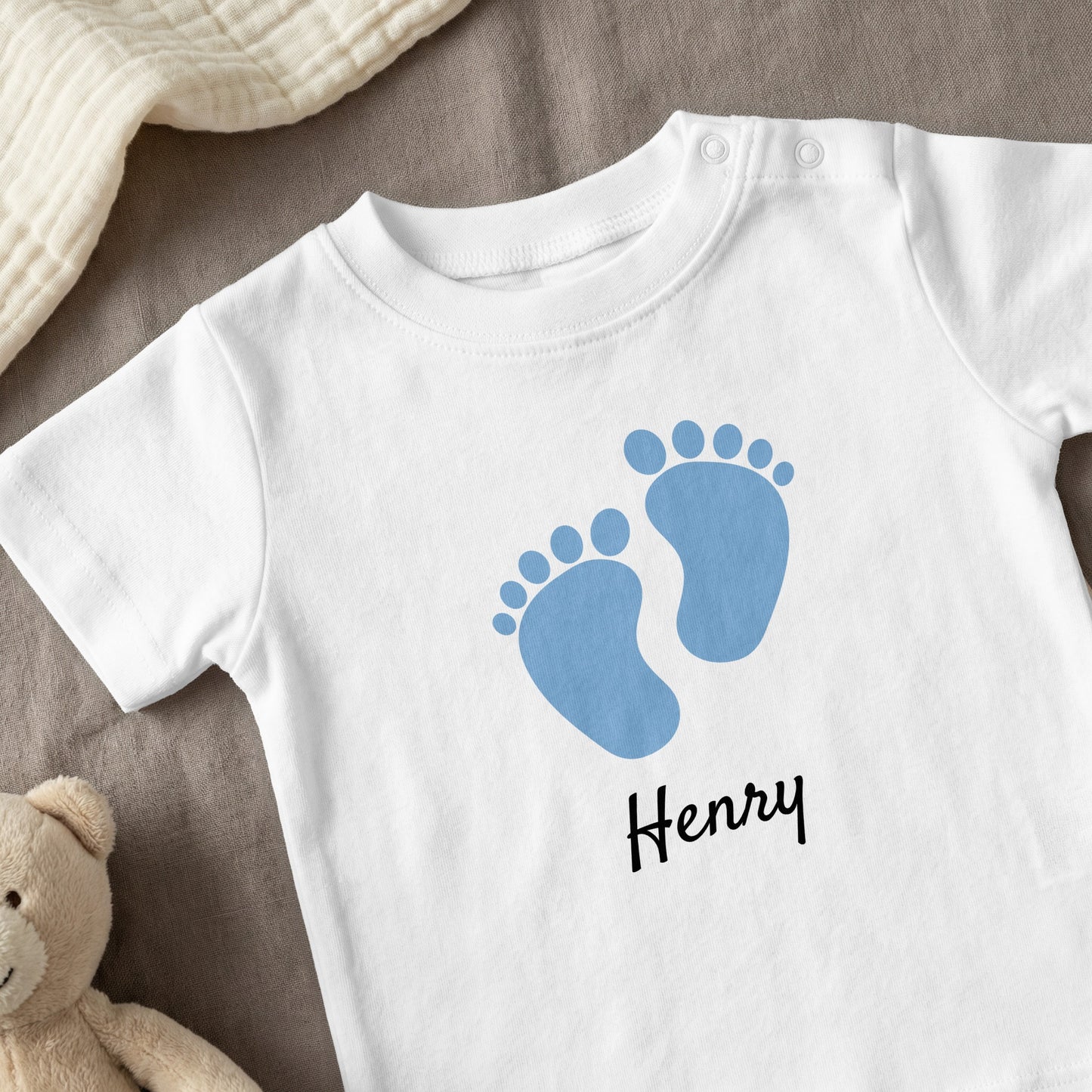 White baby onesie with blue footprints and "Henry" text.