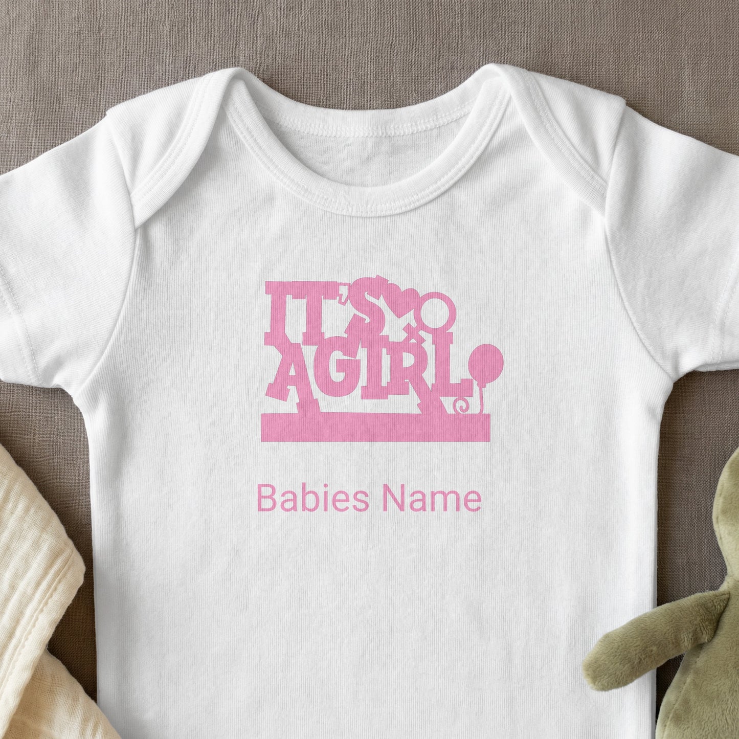 White baby onesie with "It's A Girl" and "Babies Name" text in pink.