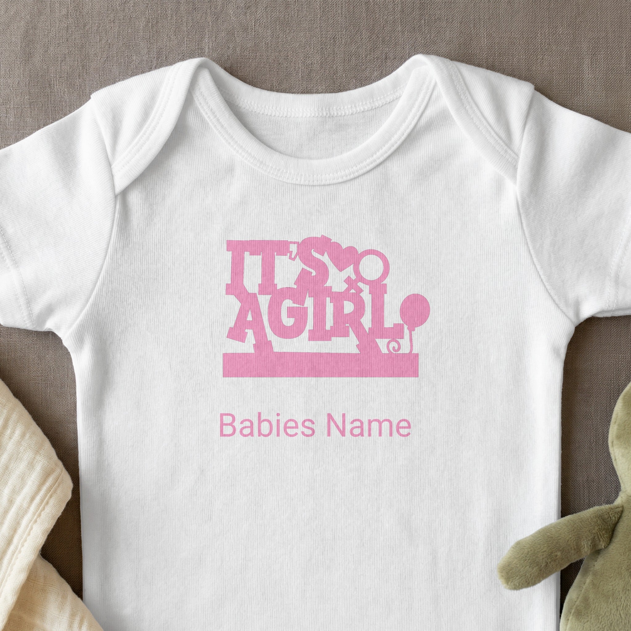 White baby onesie with "It's A Girl" and "Babies Name" text in pink.