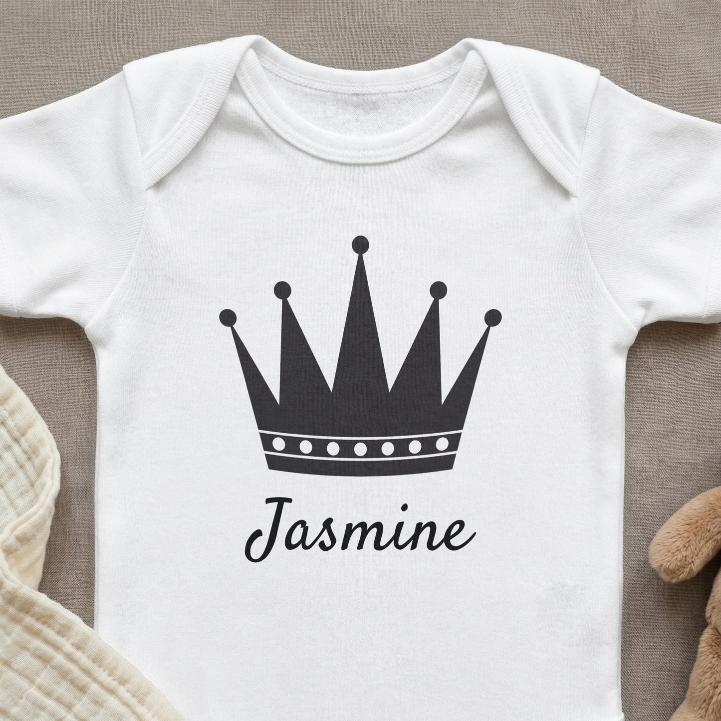 White baby onesie with a black crown and "Jasmine" text.