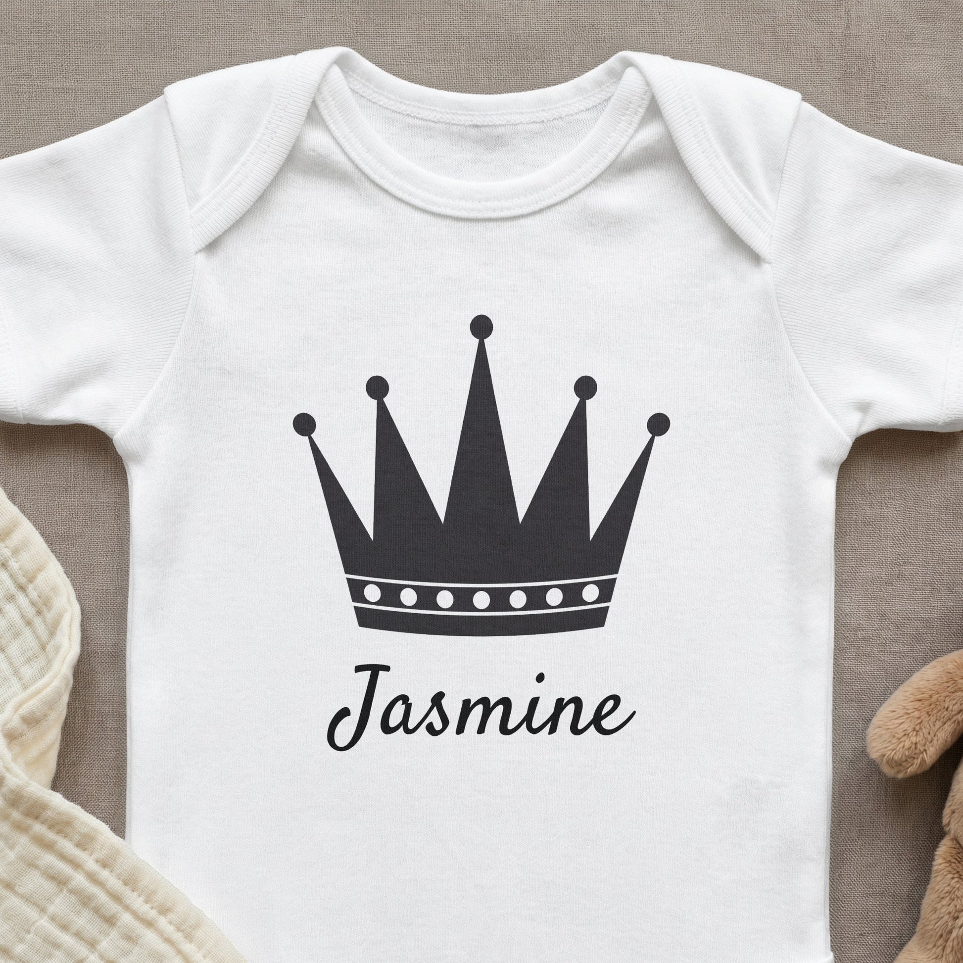 White baby onesie with a black crown and "Jasmine" text.
