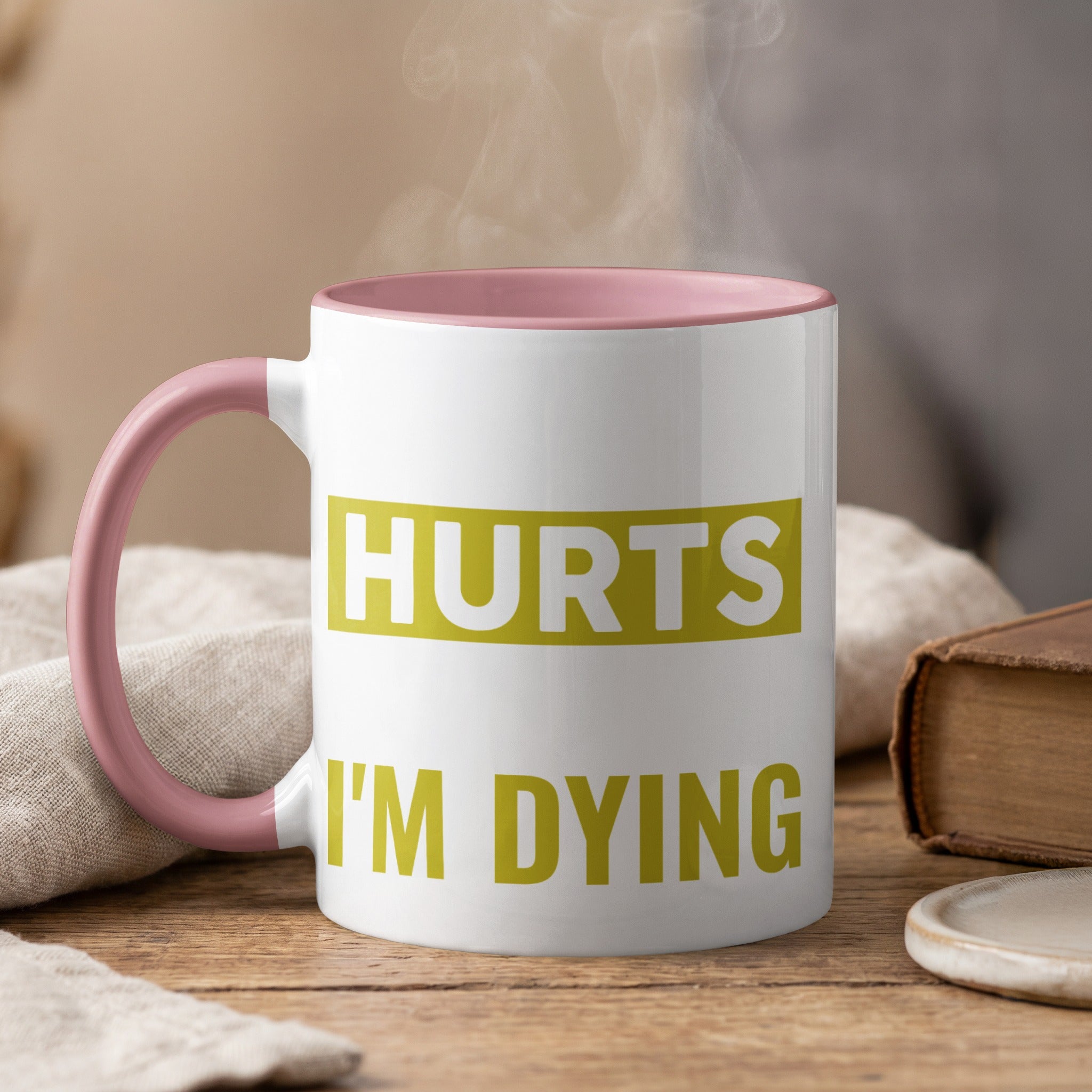 White mug with pink handle, text "HURTS I'M DYING" in green.