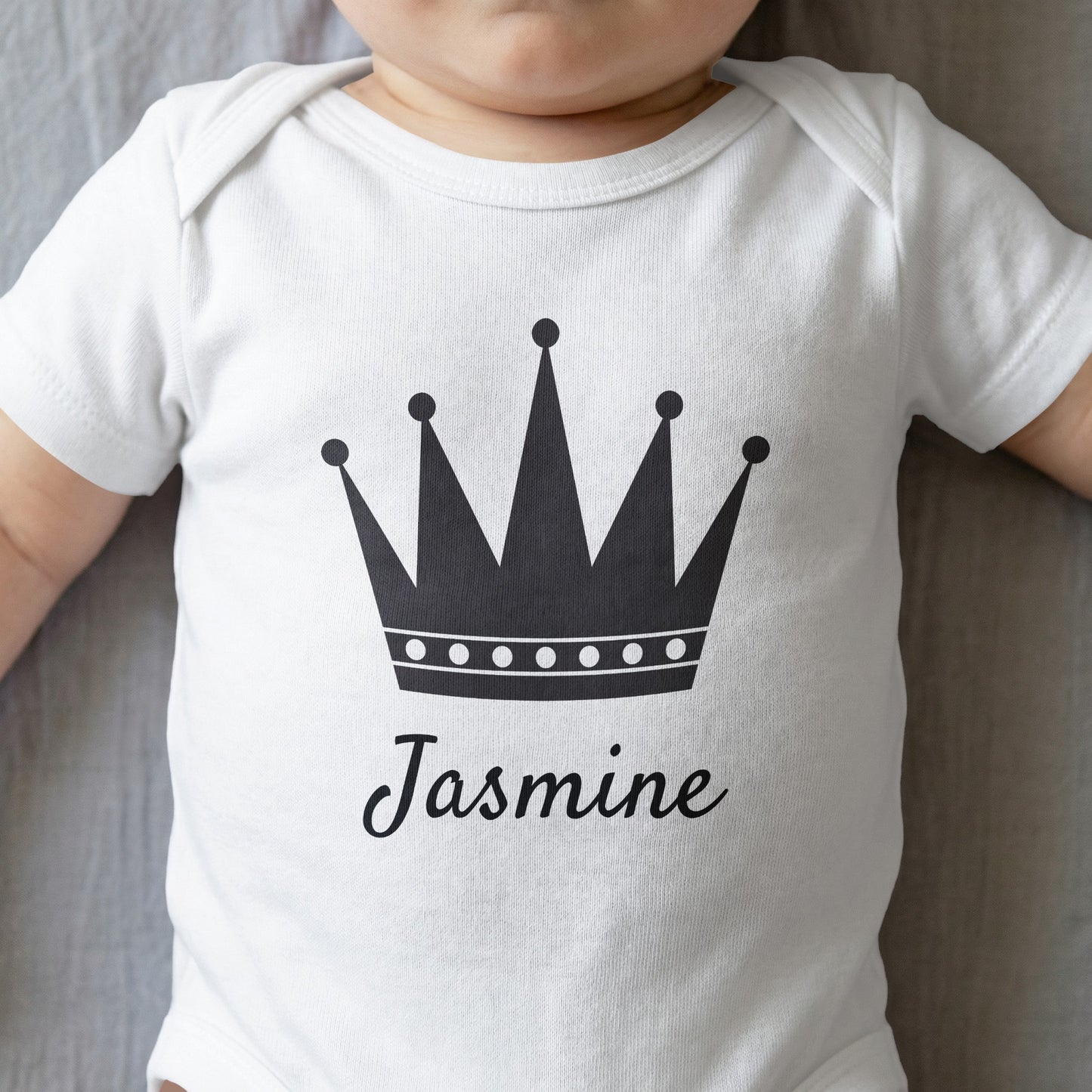 White baby onesie with a black crown and "Jasmine" text.