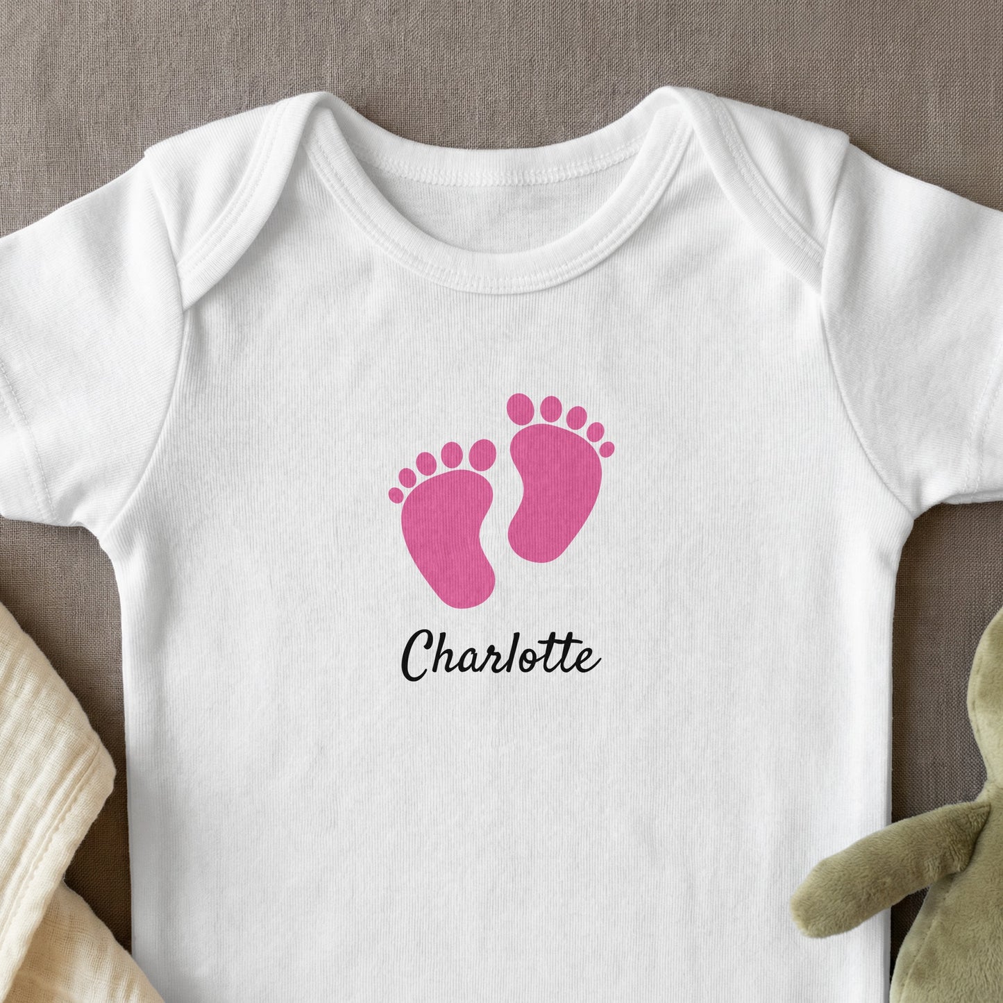 White baby onesie with pink footprints and "Charlotte" text.