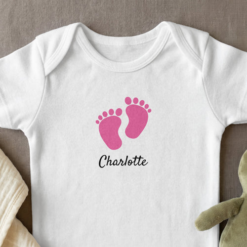 White baby onesie with pink footprints and "Charlotte" text.