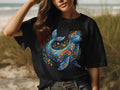 Black t-shirt featuring a blue seal adorned with colorful floral patterns.