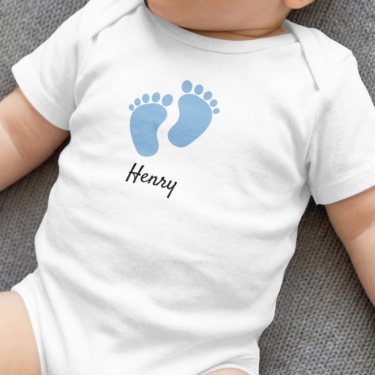 White baby onesie with blue footprints and "Henry" text.