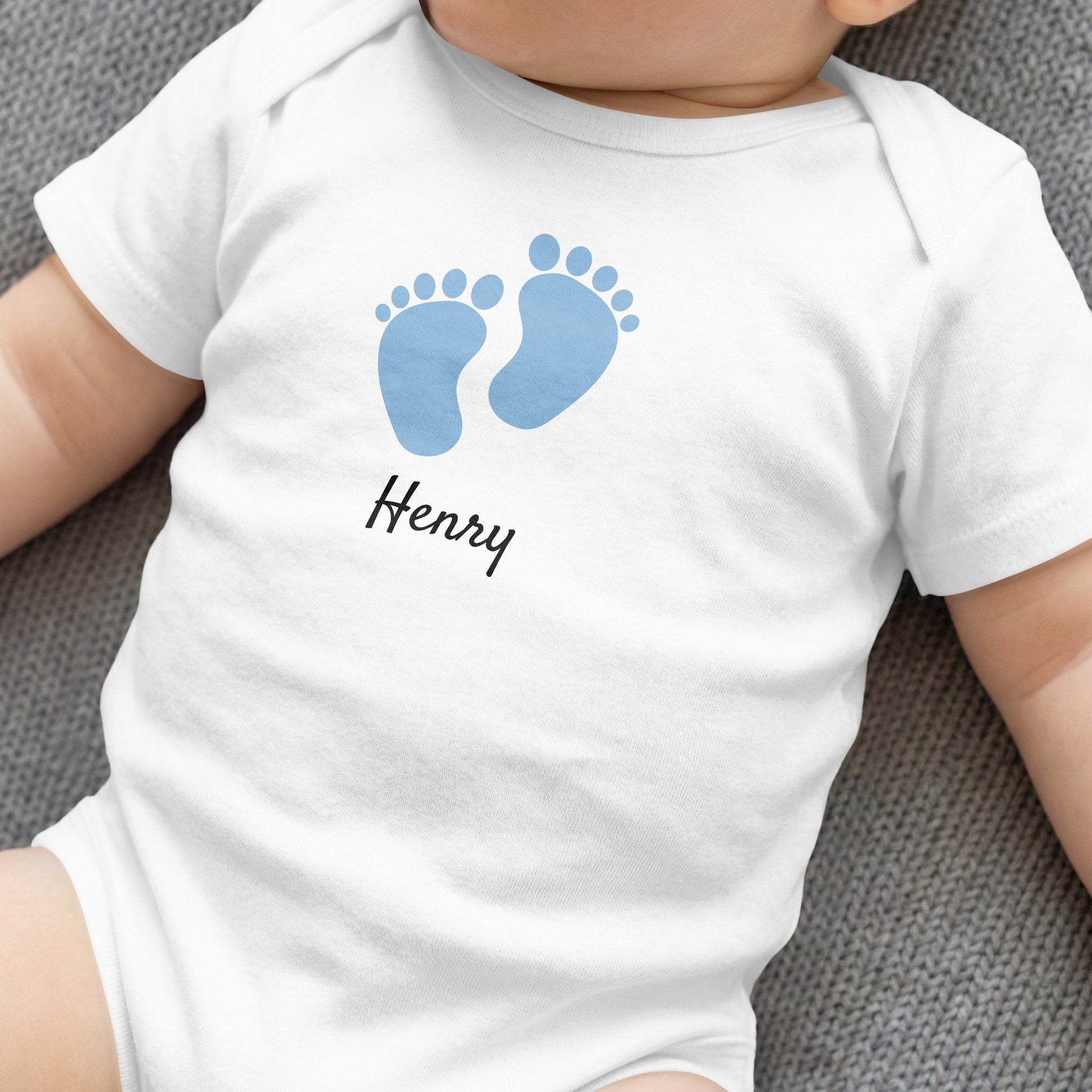 White baby onesie with blue footprints and "Henry" text.