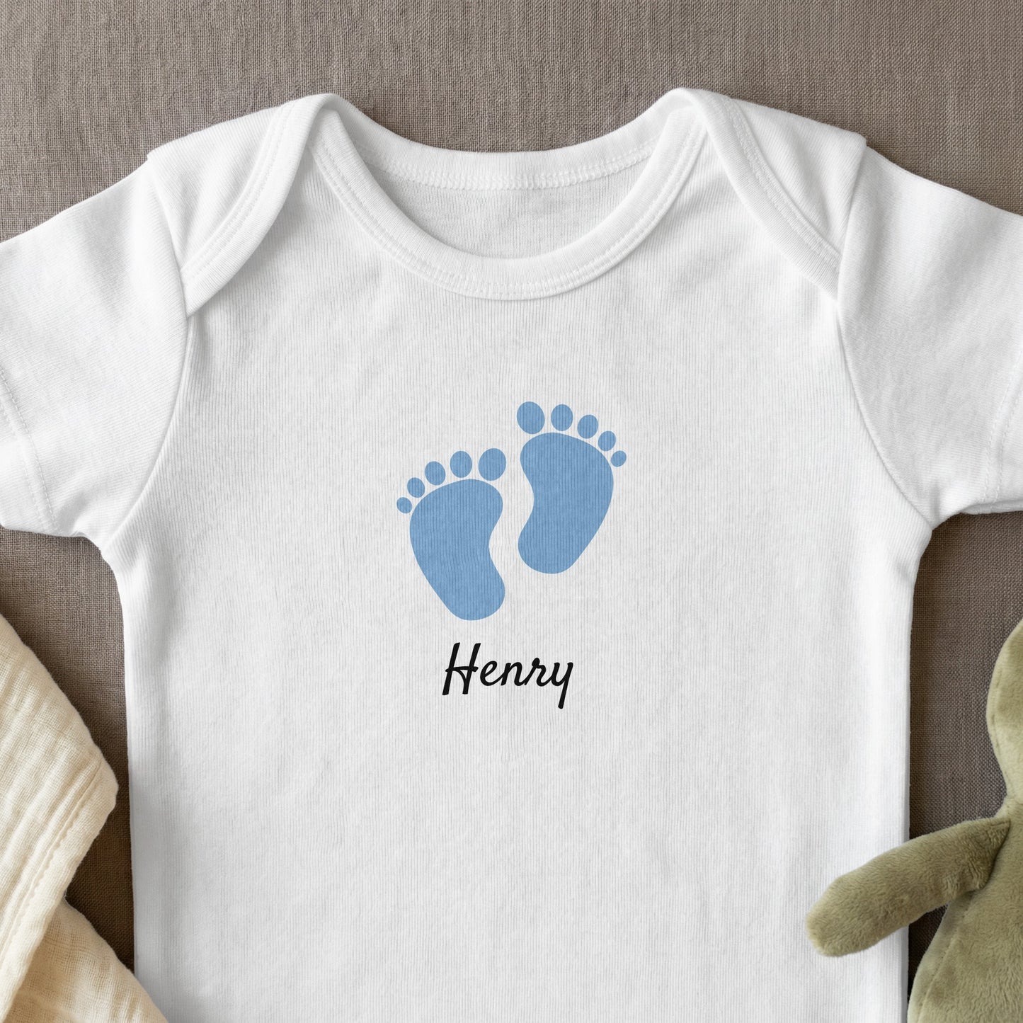 White baby onesie with blue footprints and "Henry" text.