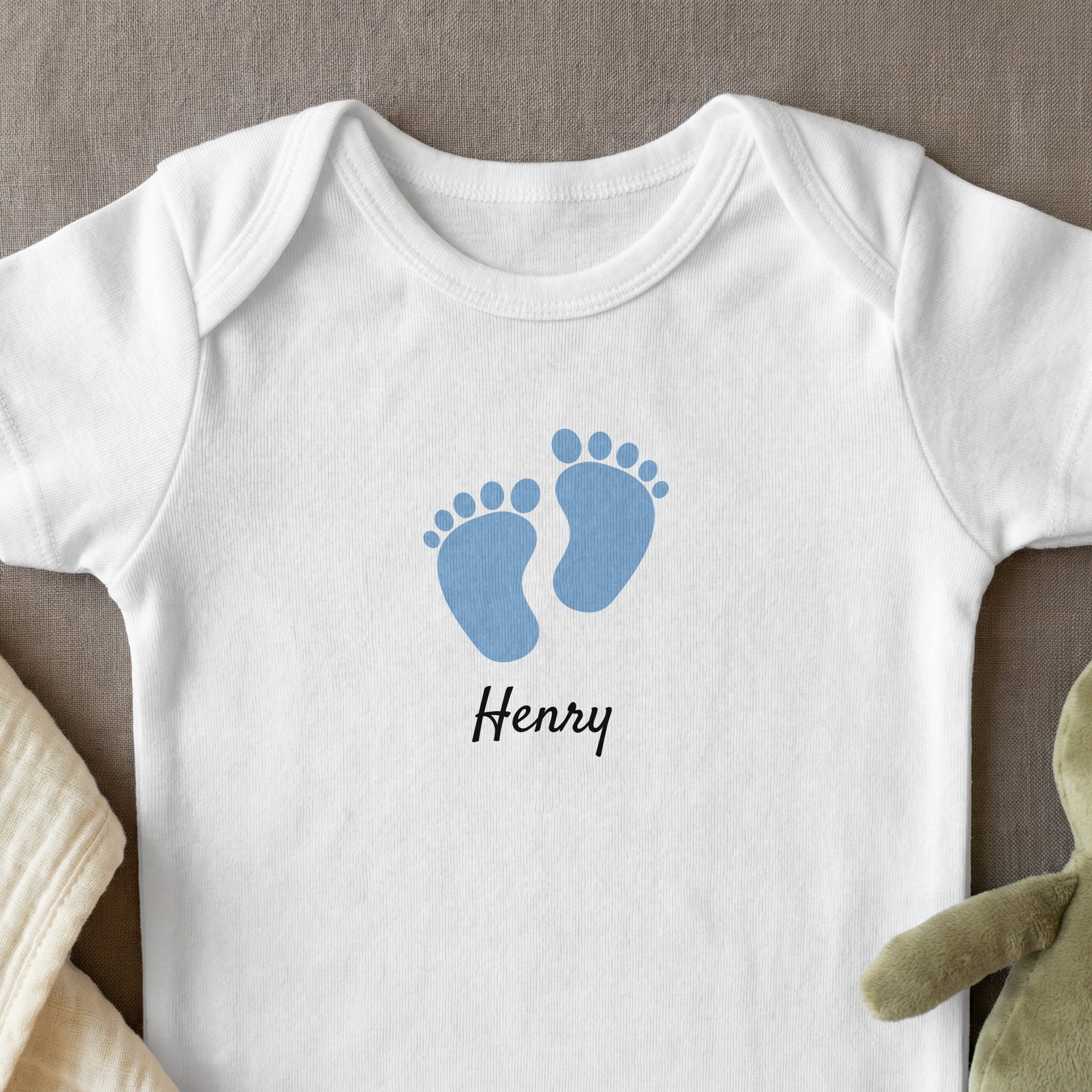 White baby onesie with blue footprints and "Henry" text.