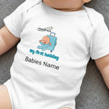 Baby bodysuit with airplane, suitcase, and "my first holiday" text.