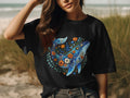 Black t-shirt with a blue whale design surrounded by colorful flowers.