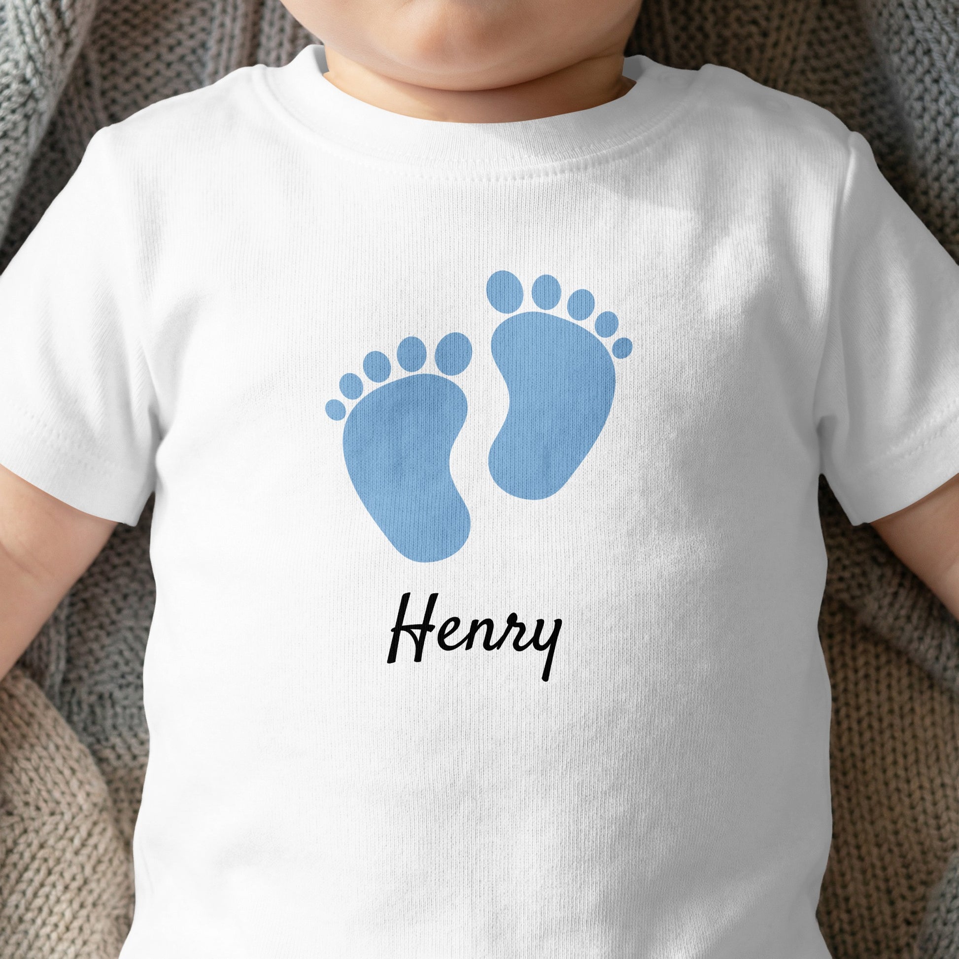 White baby t-shirt with blue footprints and "Henry" text.